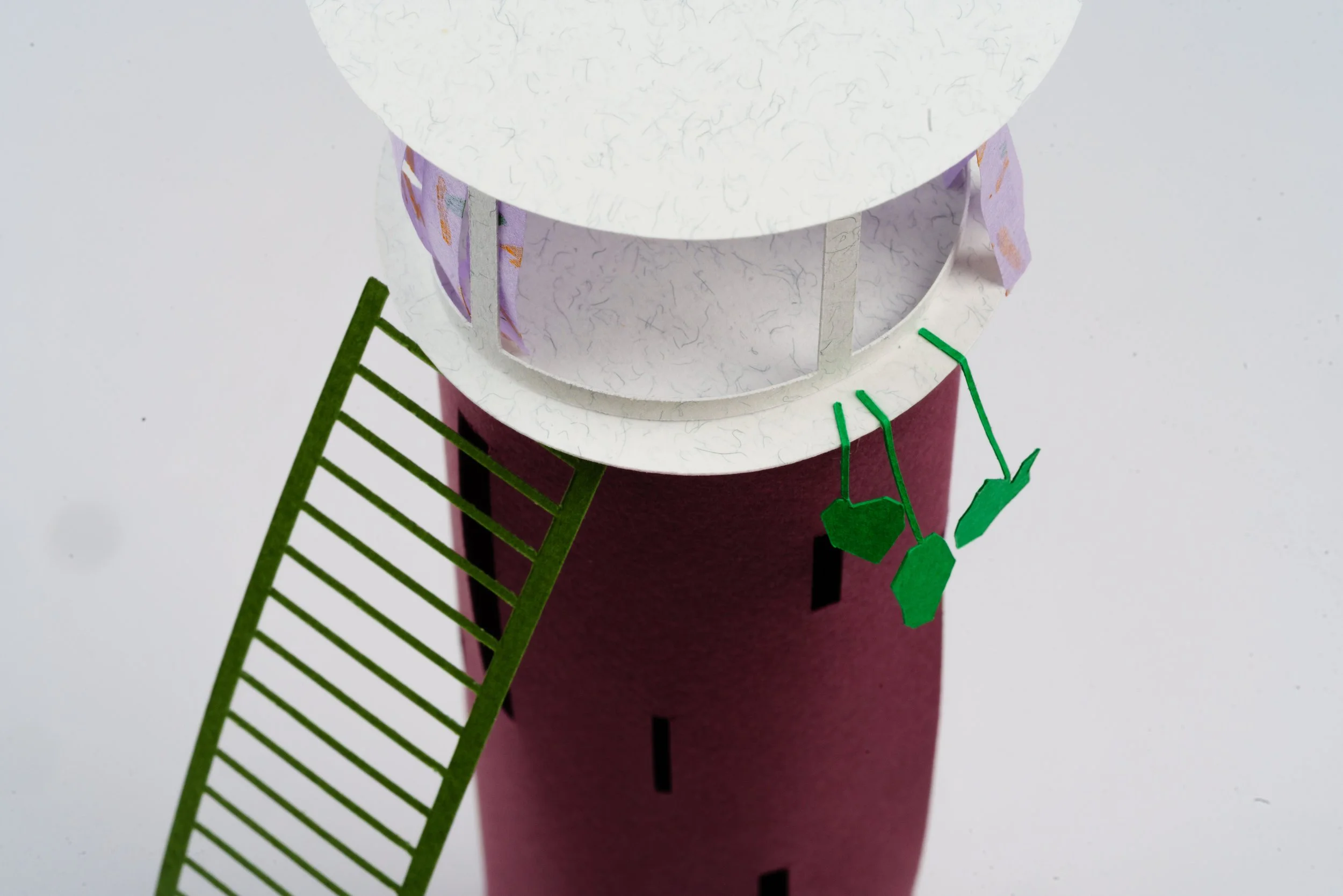 A paper model of a multi-tiered tower with a white top, purple middle, and red bottom, decorated with small green paper plants and a green paper ladder leaning against it, set against a plain background.