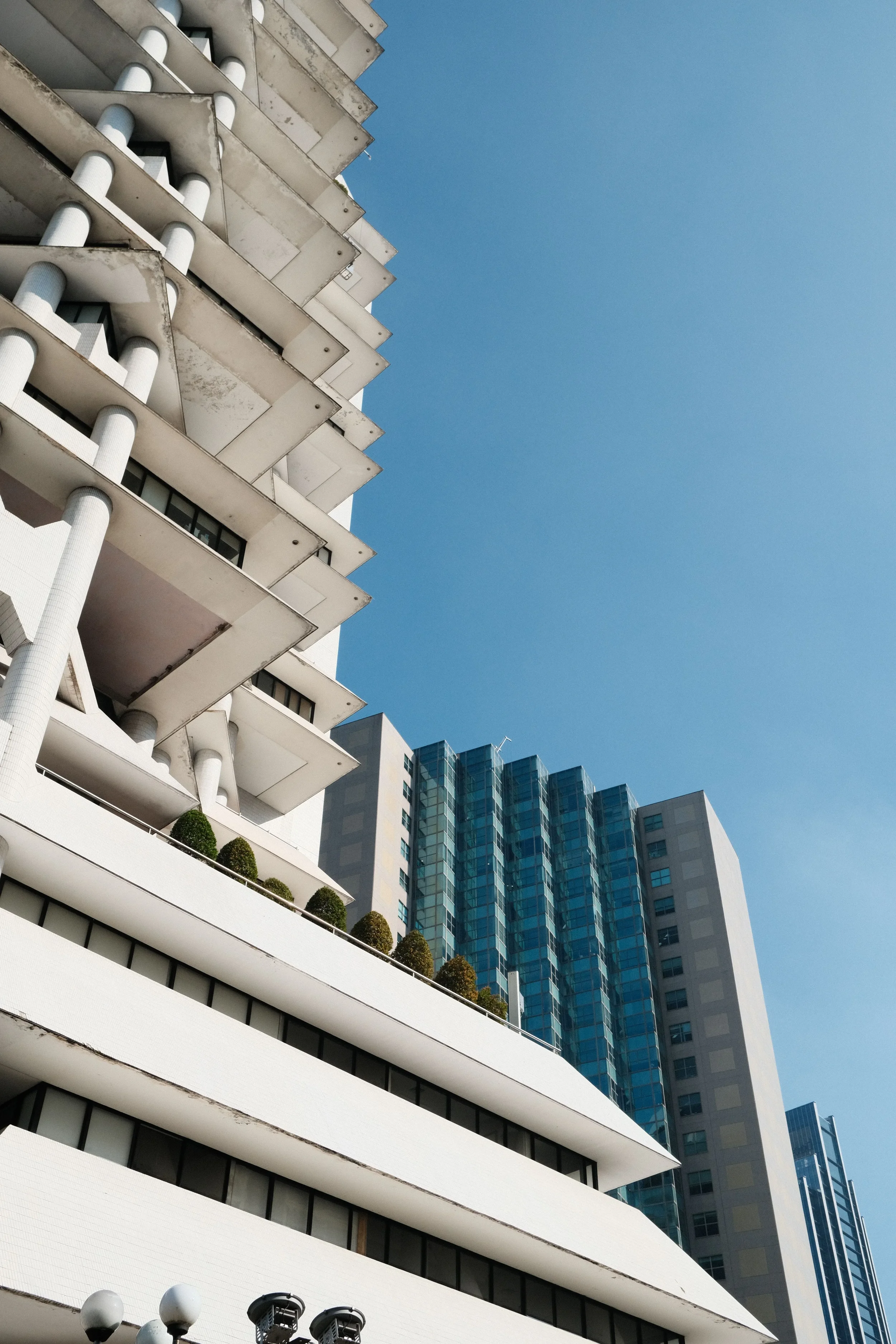A tall modern building with multiple balconies and a white facade, with a clear blue sky in the background.