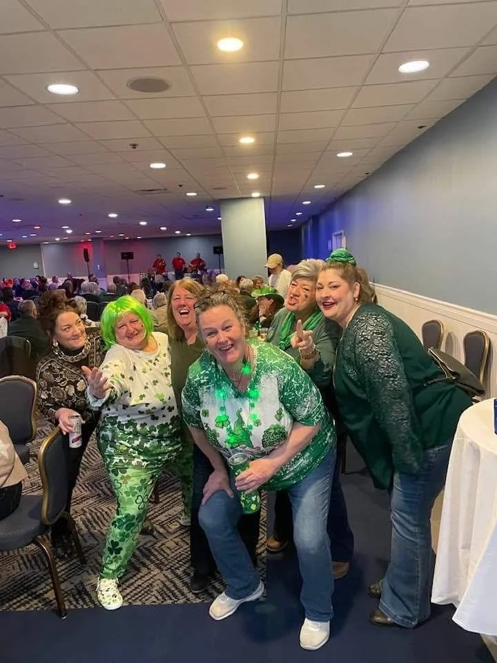 Group of people dressed in green posing and smiling at an indoor event.