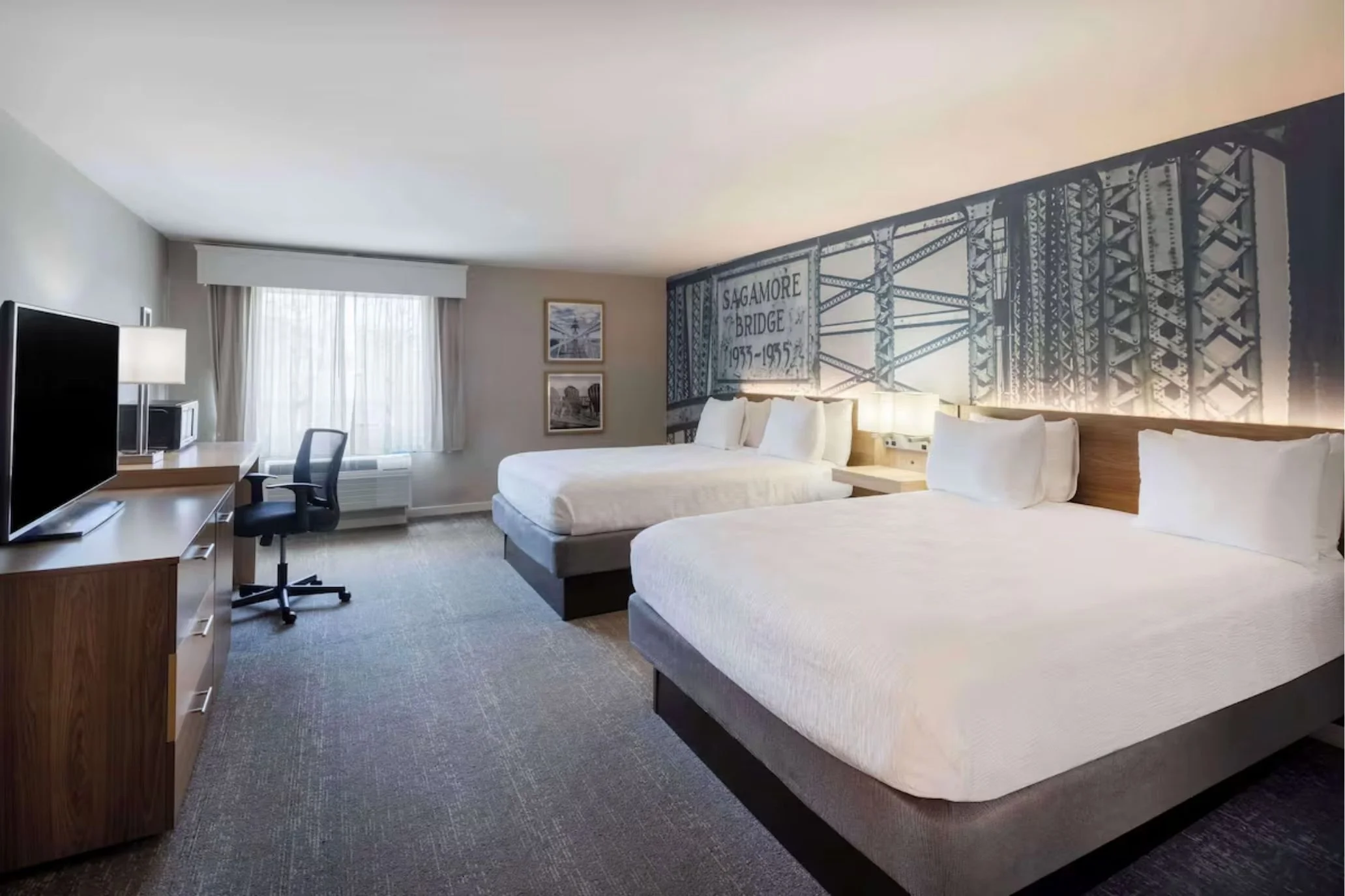 Contemporary guest room with two queen beds, desk, television, and large window.