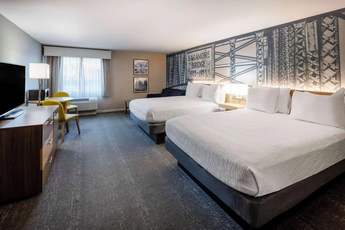 Spacious hotel room with two queen beds and contemporary decor.