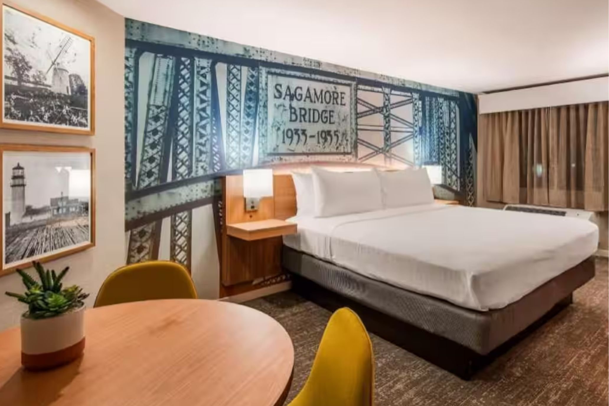 Modern hotel guest room with a king bed, seating area, and Sagamore Bridge mural accent wall.