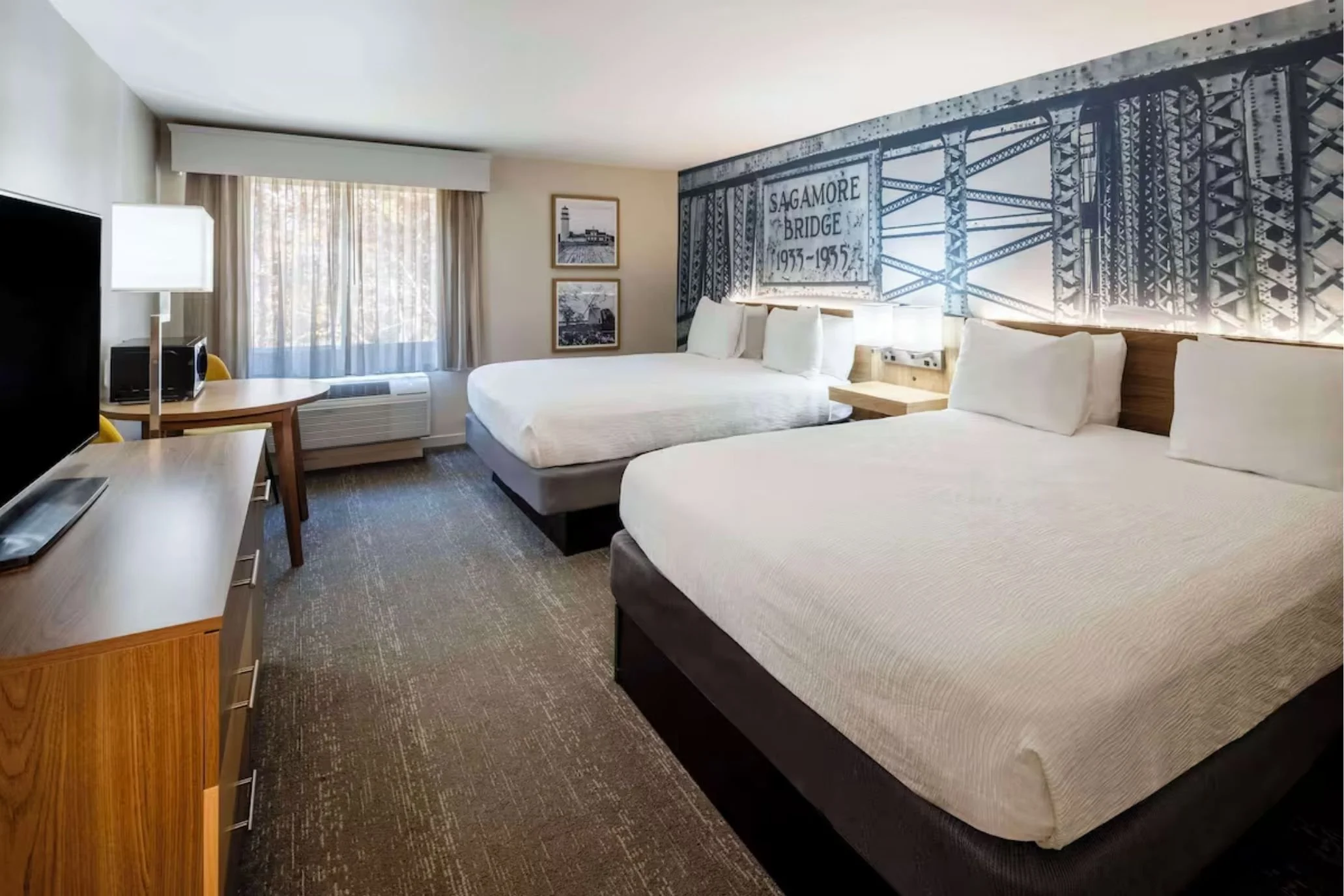 Spacious hotel room featuring two queen beds, a work area, and a bridge-themed wall mural.