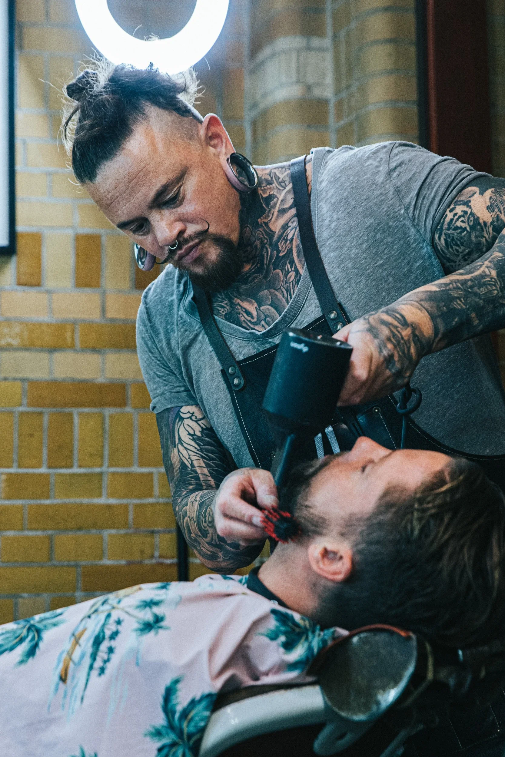 Een barbier geeft een man een scheerbeurt in een barbershop. De man ligt in een barberstoel met een bloemmotief op zijn kussensloop.