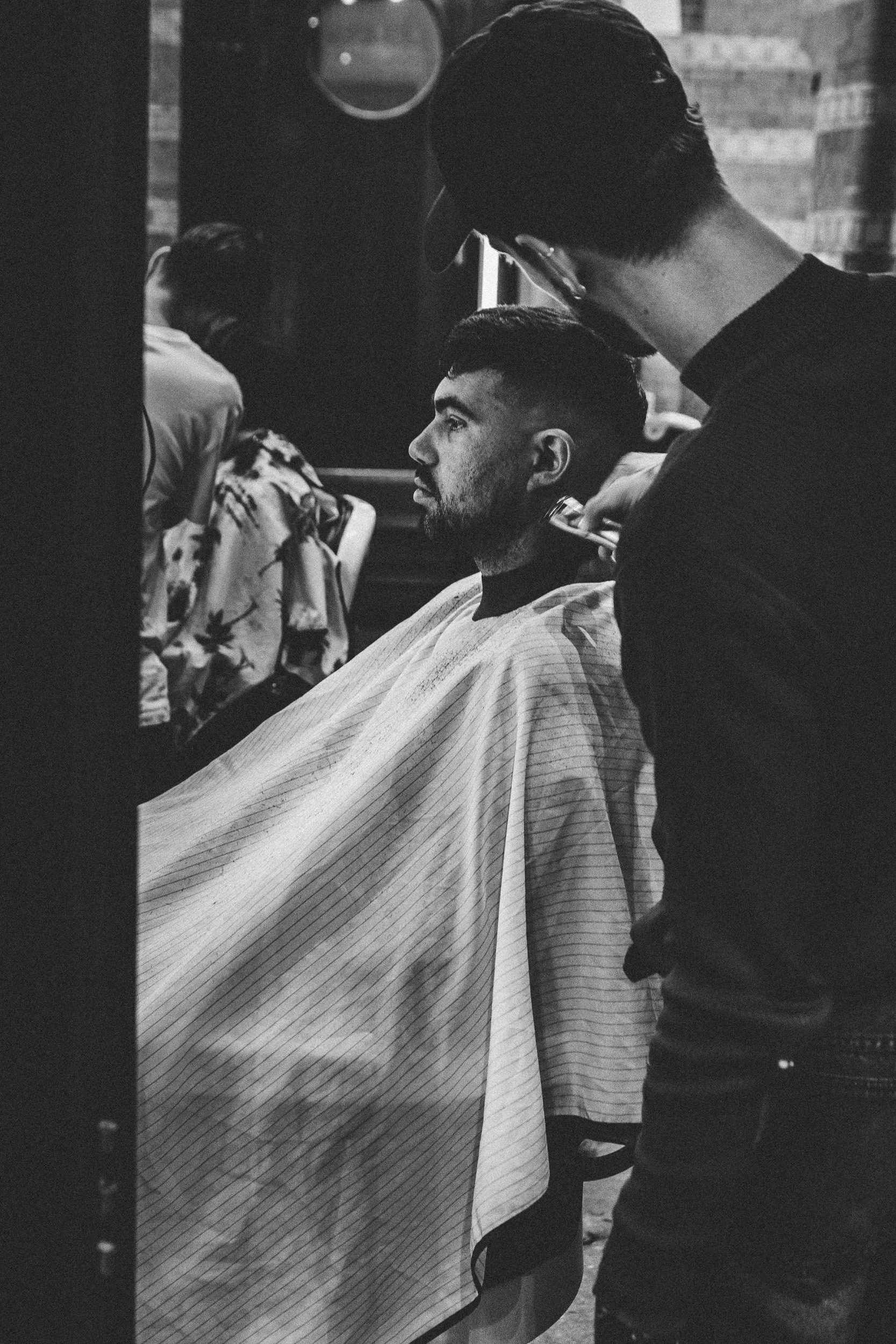 Klassieke zwart-wit bedrijfsfotografie van een barbier aan het werk in zijn salon. Authentieke ambachtsfotografie en karakterportret.