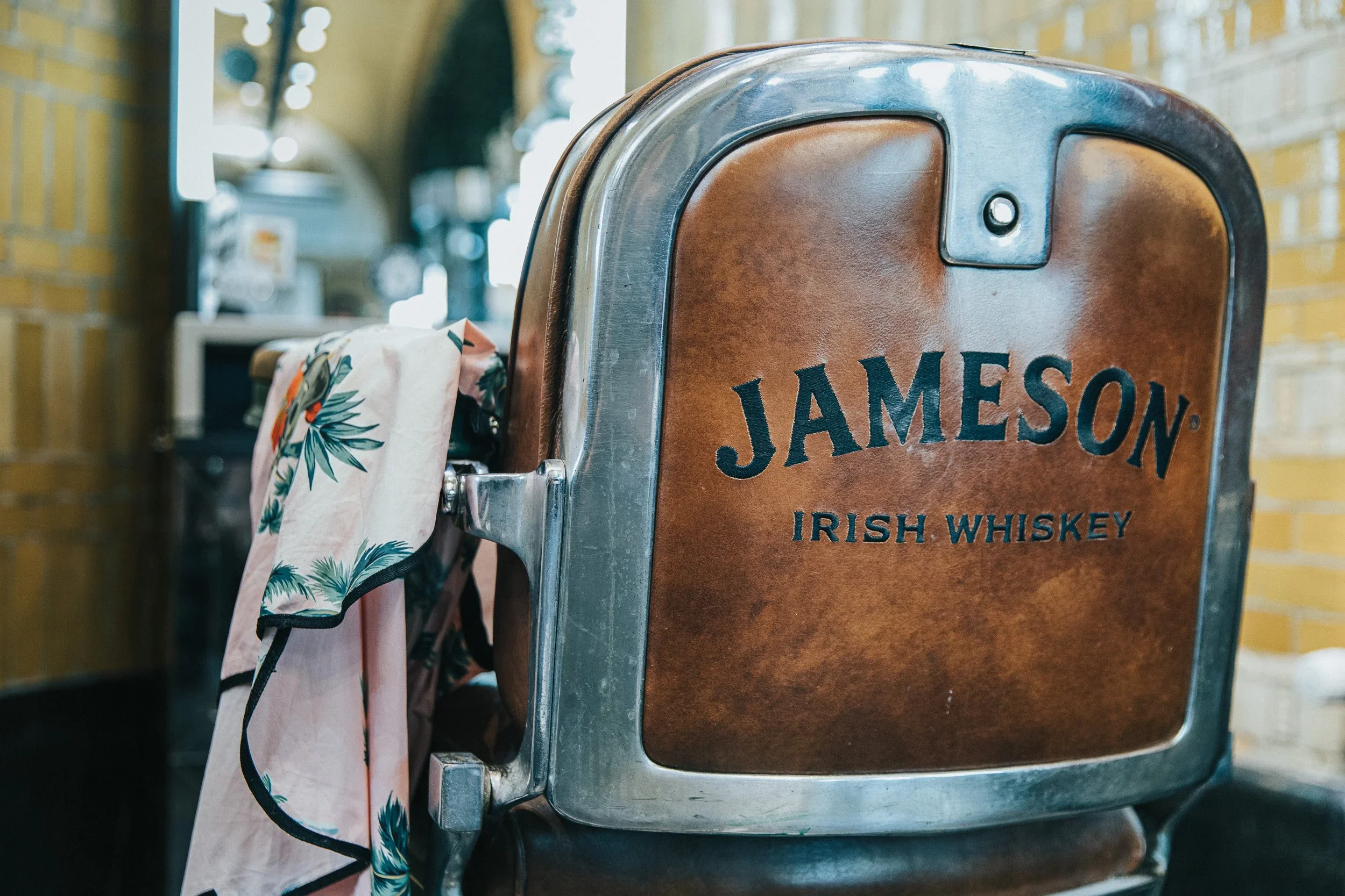 De afbeelding toont een roestvrijstalen muur met een houten bankje dat de tekst 'Jameson Irish Whiskey' draagt.