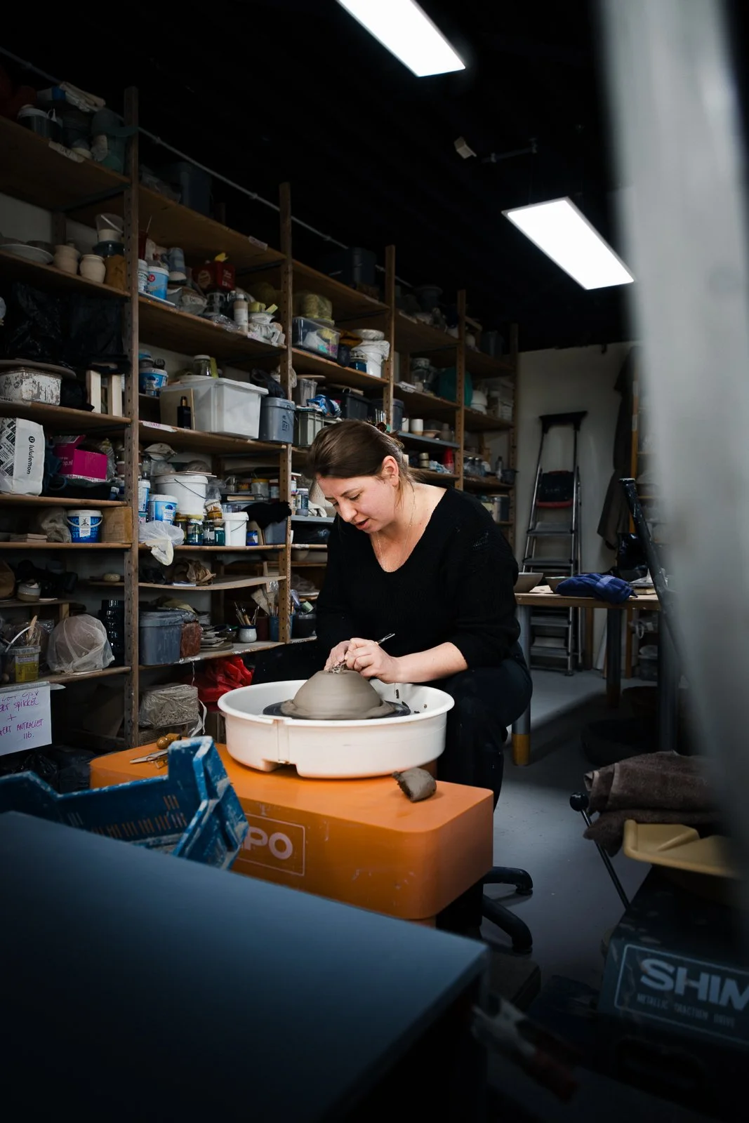 Vrouw die pottenbakken in een atelier met opbergkasten vol keramiek- en kunstbenodigdheden.