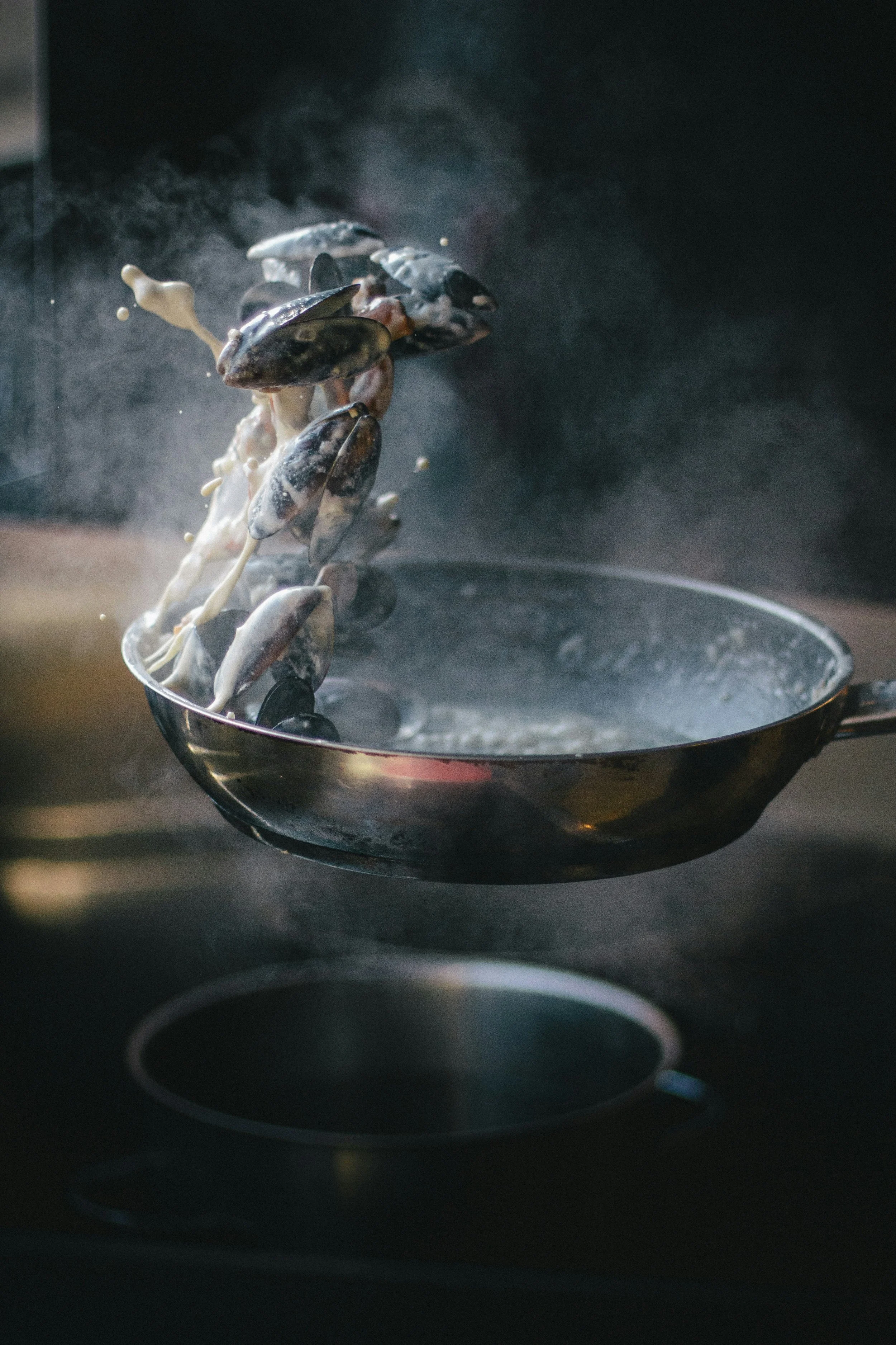 Mussels cooking in a steaming pan with steam and sauce mist