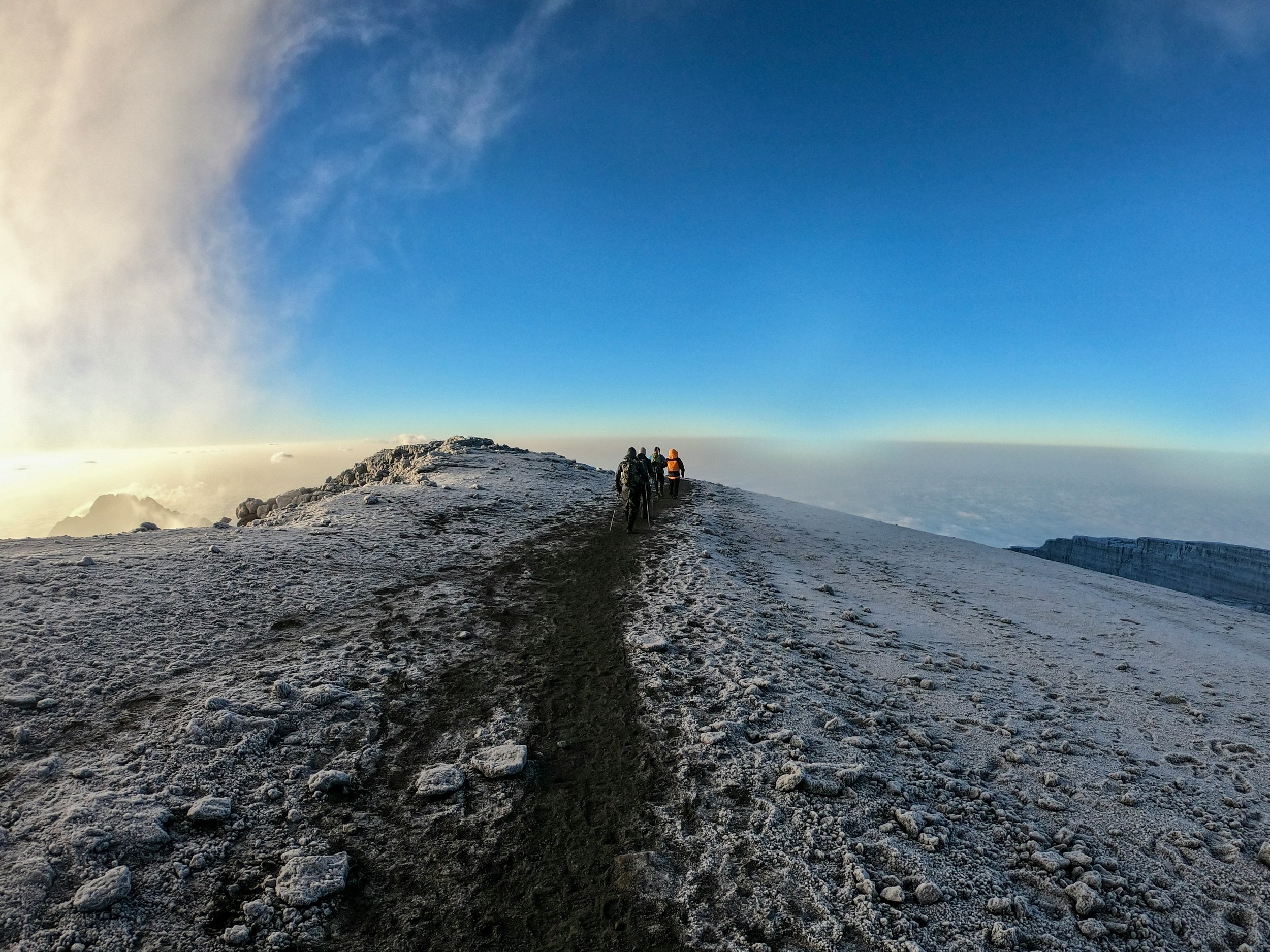 Group of hikers walking on a rocky mountain trail in Africa above the clouds under a blue sky.
