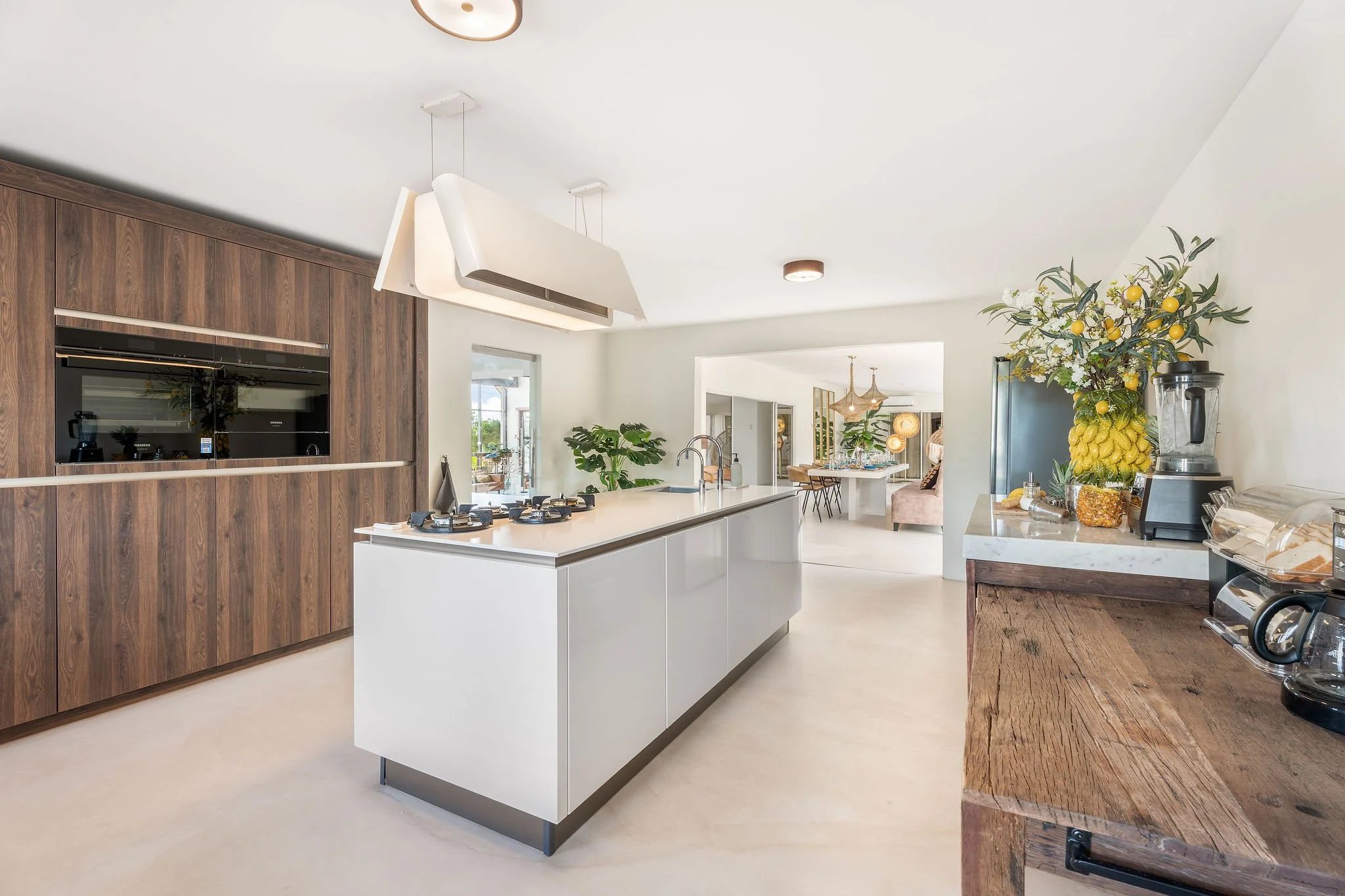 Modern kitchen with white island, wooden cabinetry, and decorative fruit arrangement on a blender