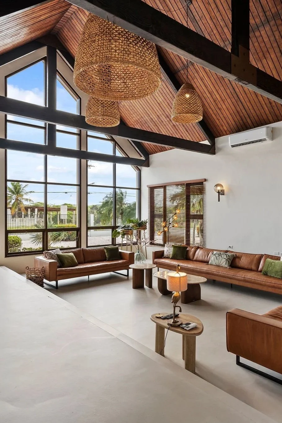 Living room with large windows, wooden ceiling, pendant lights, and leather sofas with pillows.