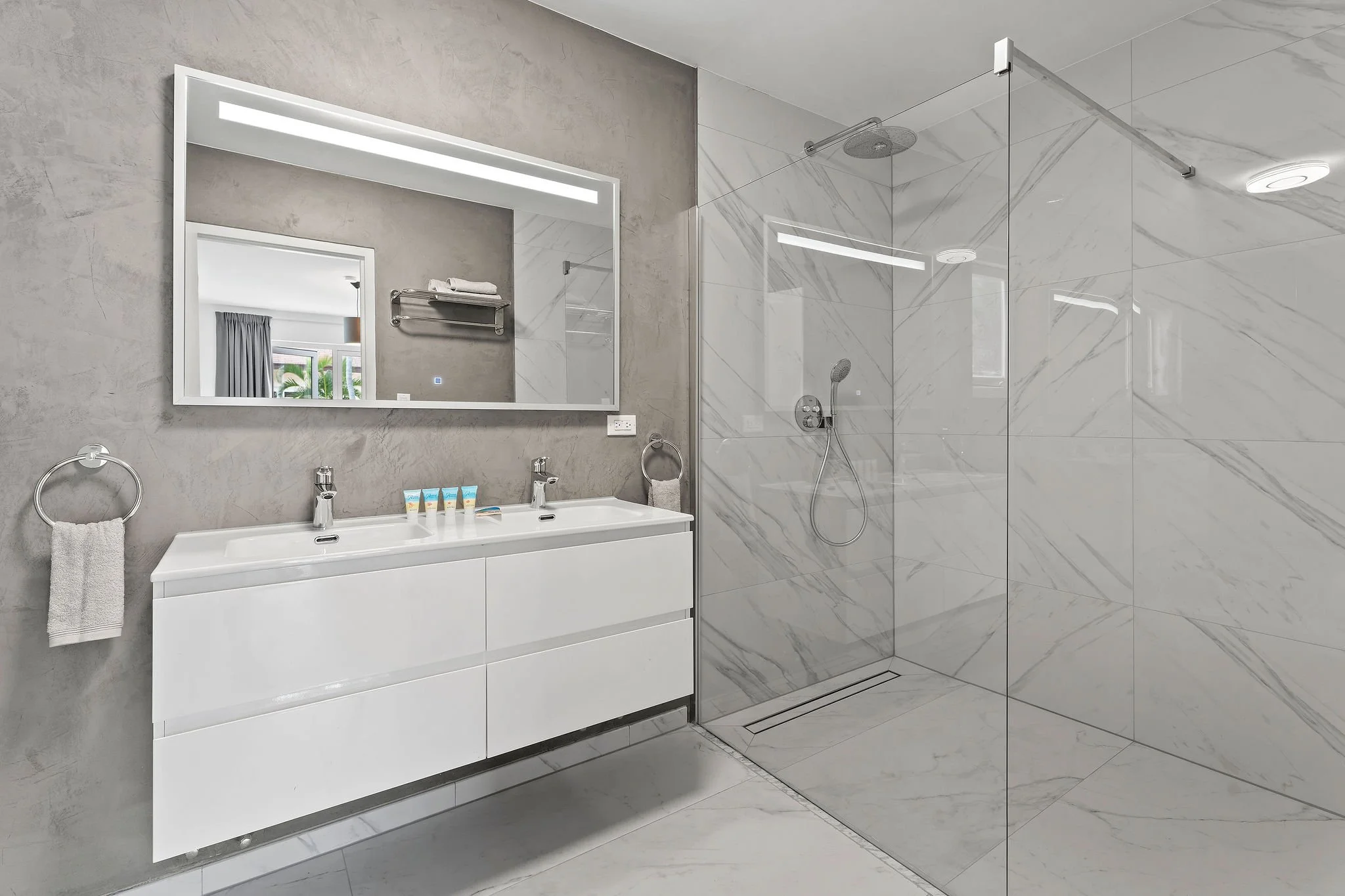 Modern bathroom with a white vanity, rectangular mirror, and a spacious glass-enclosed shower with marble tiles.