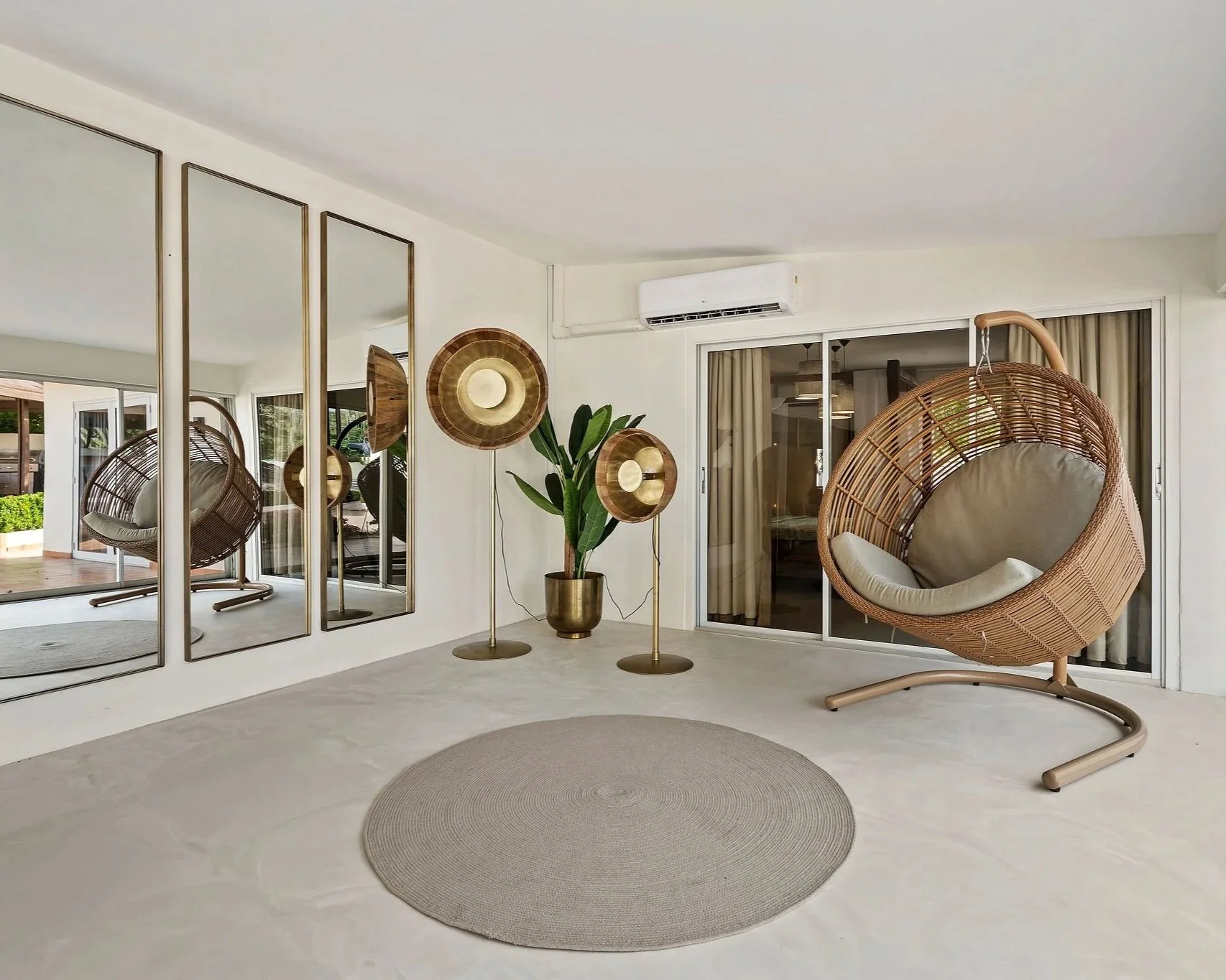 Living room with hanging egg chair, large wall mirrors, a potted plant, and modern decor including gold accents and beige tones.