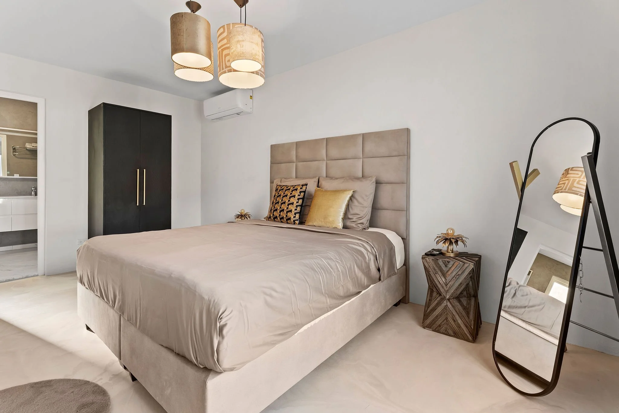 Modern bedroom with beige upholstered bed, decorative pillows, black wardrobe, hanging beige pendant lights, full-length mirror, and small wooden side table.
