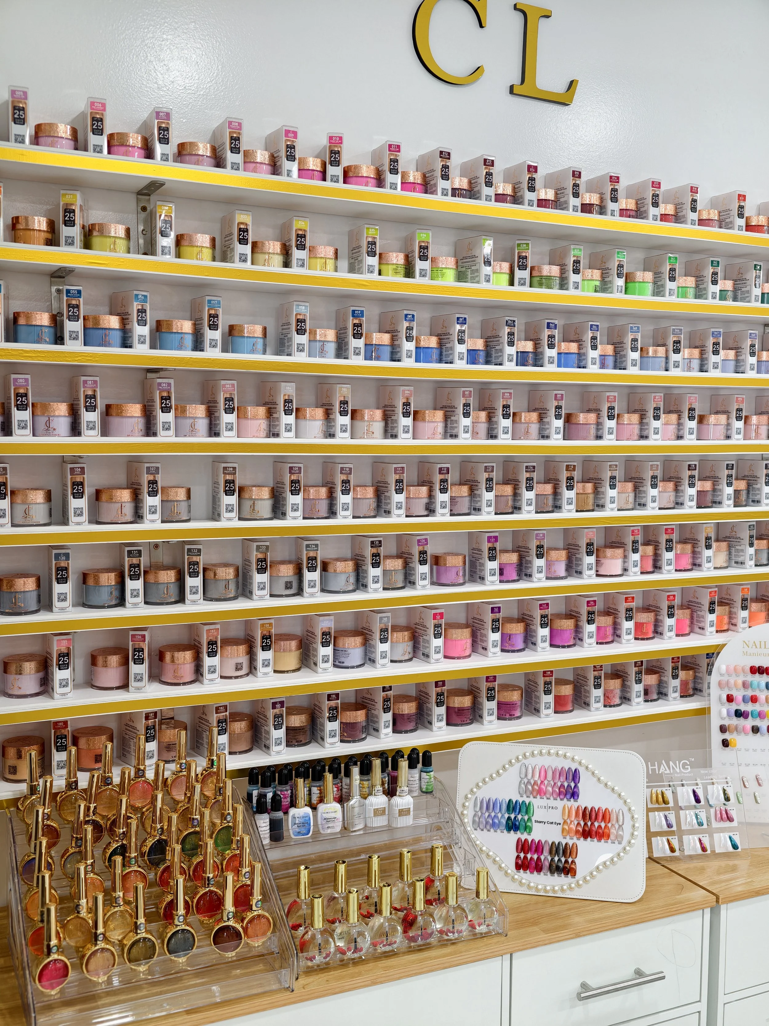 Display of multiple shelves filled with various nail polish bottles in a nail salon, with organized color arrangements and nail polish swatches on a heart-shaped board.