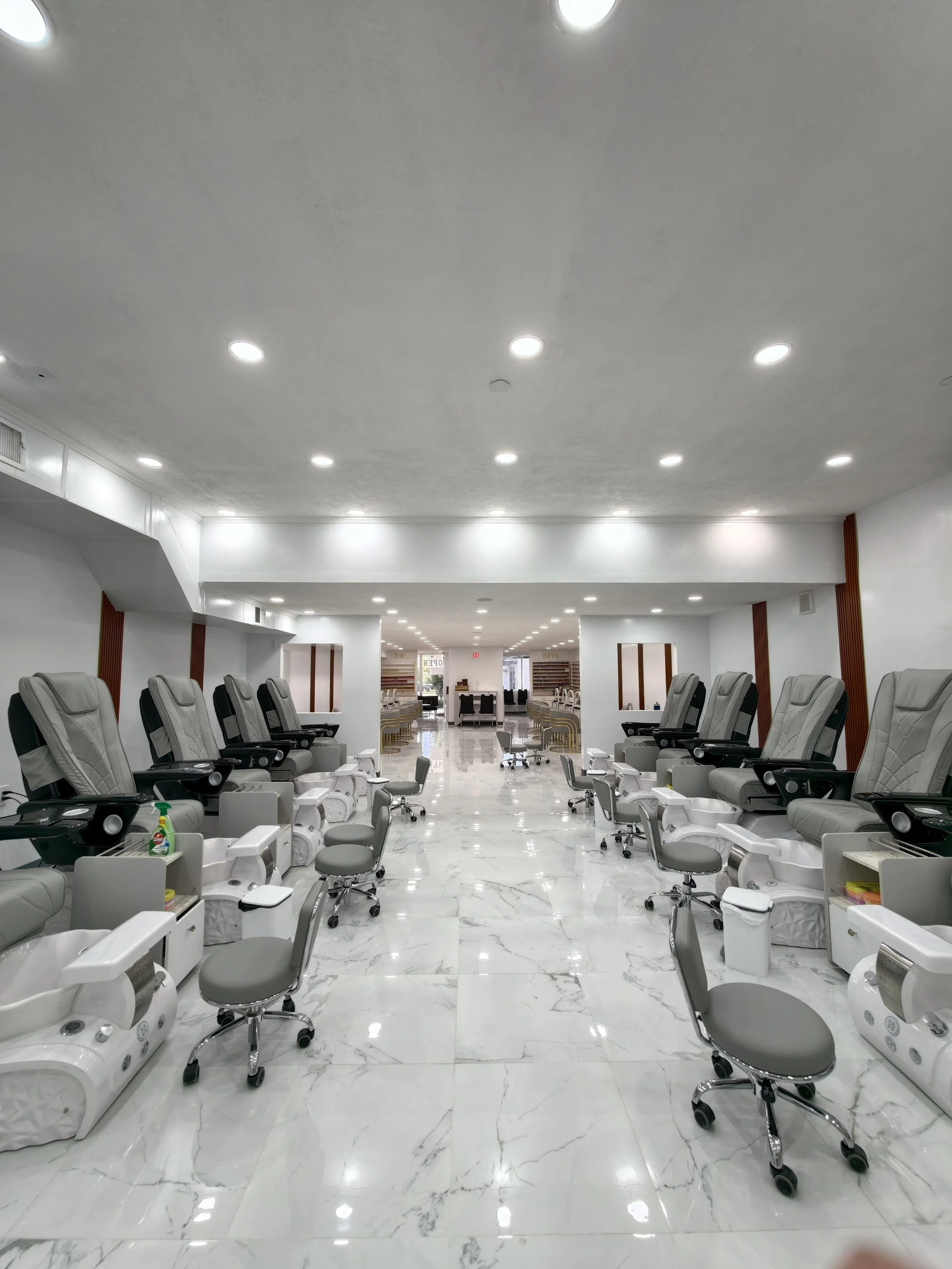 A modern salon or beauty spa with multiple reclining chairs, pedicure stations, and a clean, bright interior with marble flooring and white walls.