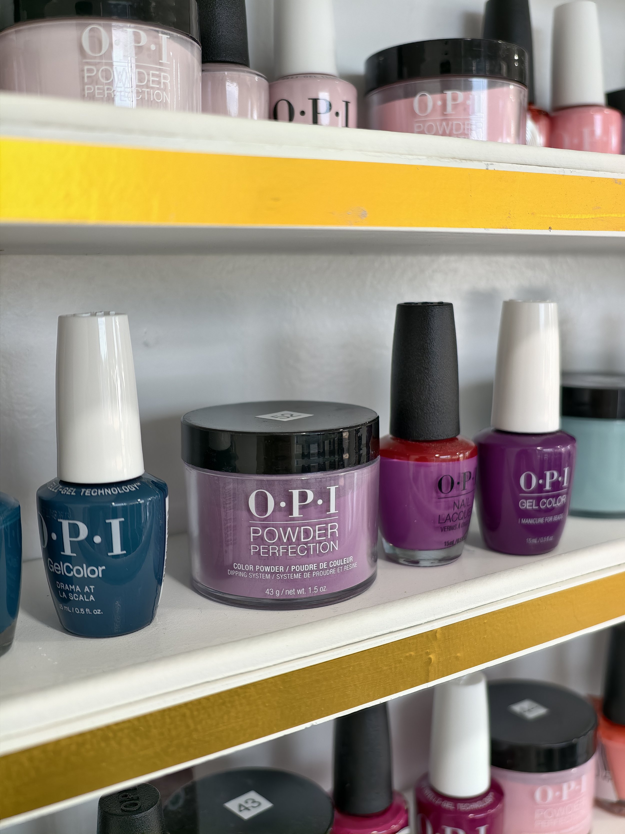 Several bottles of OPI nail polish in various colors, including blue, pink, purple, black, and white, arranged on a store shelf.