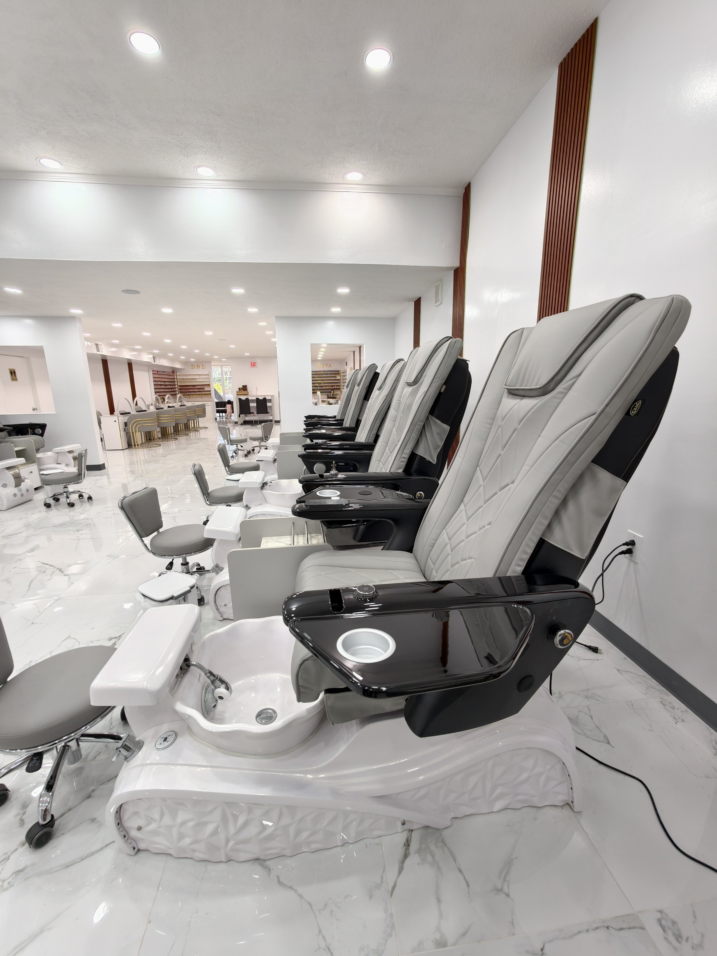 Multiple massage chairs and foot baths in a salon or spa with white walls and marble floors.