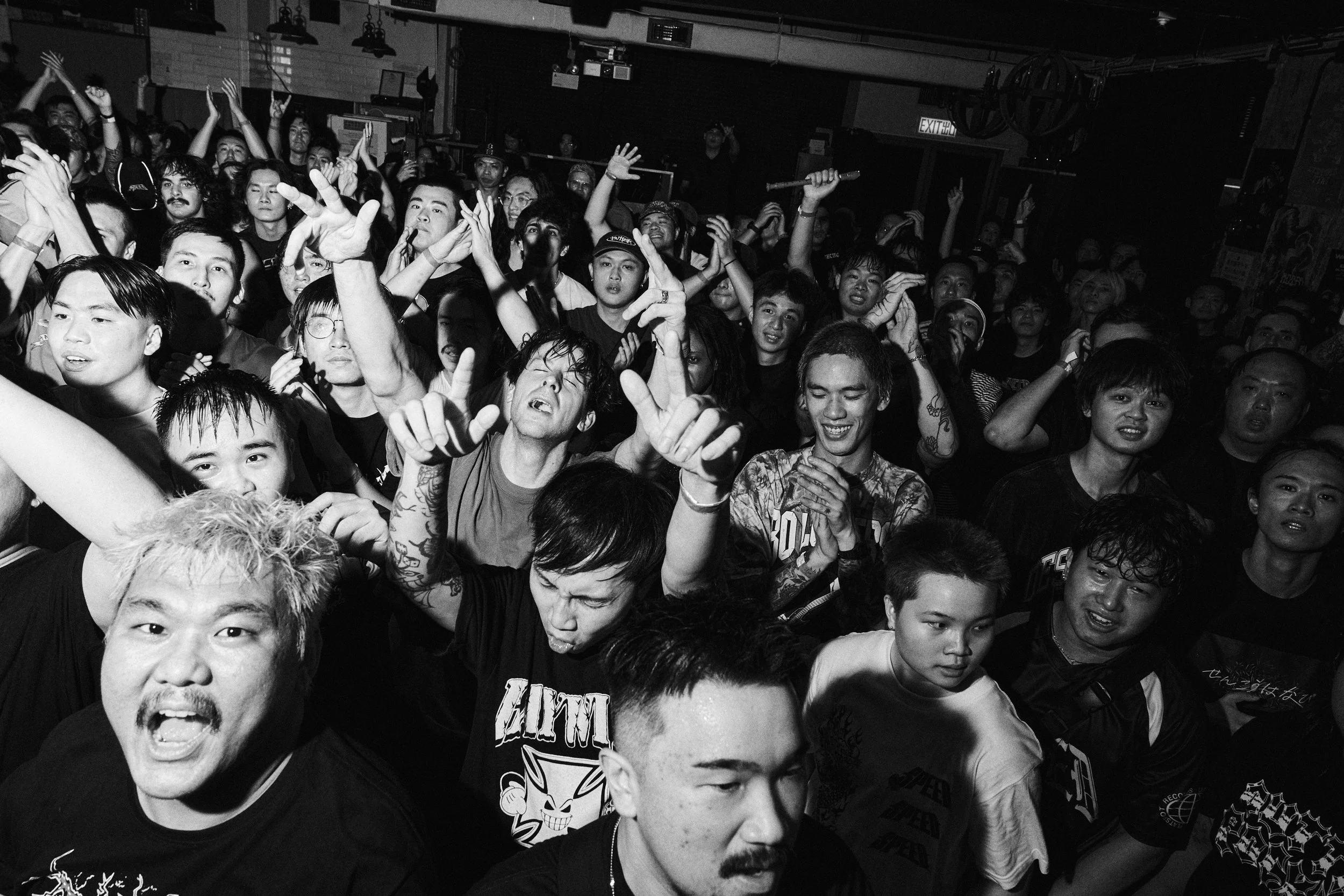 A crowded indoor concert or club scene with diverse people dancing and enjoying music, some raising their hands or taking photos.