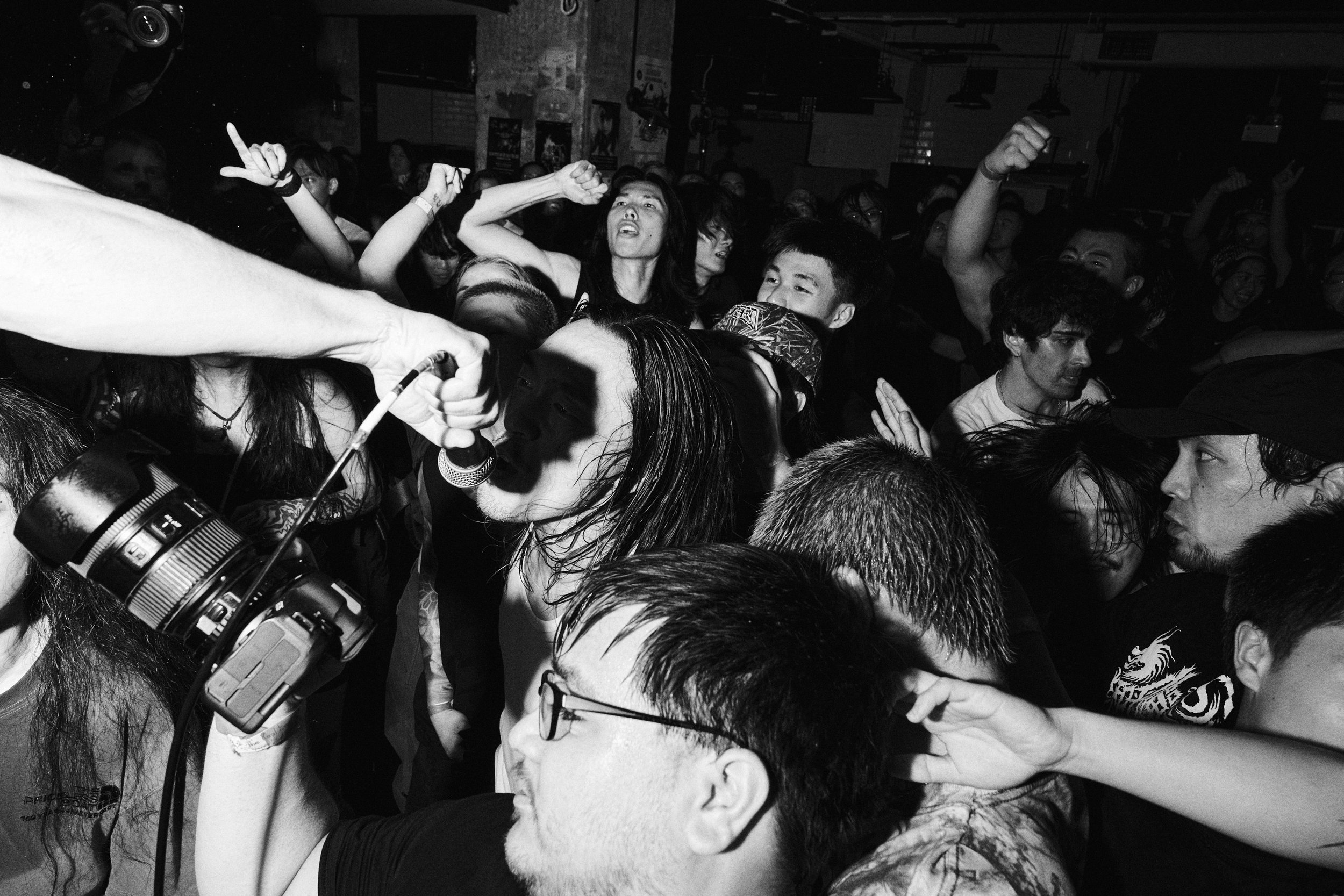 A black and white photo of a crowded concert or event with people dancing and enjoying themselves, some raising their hands and singing.