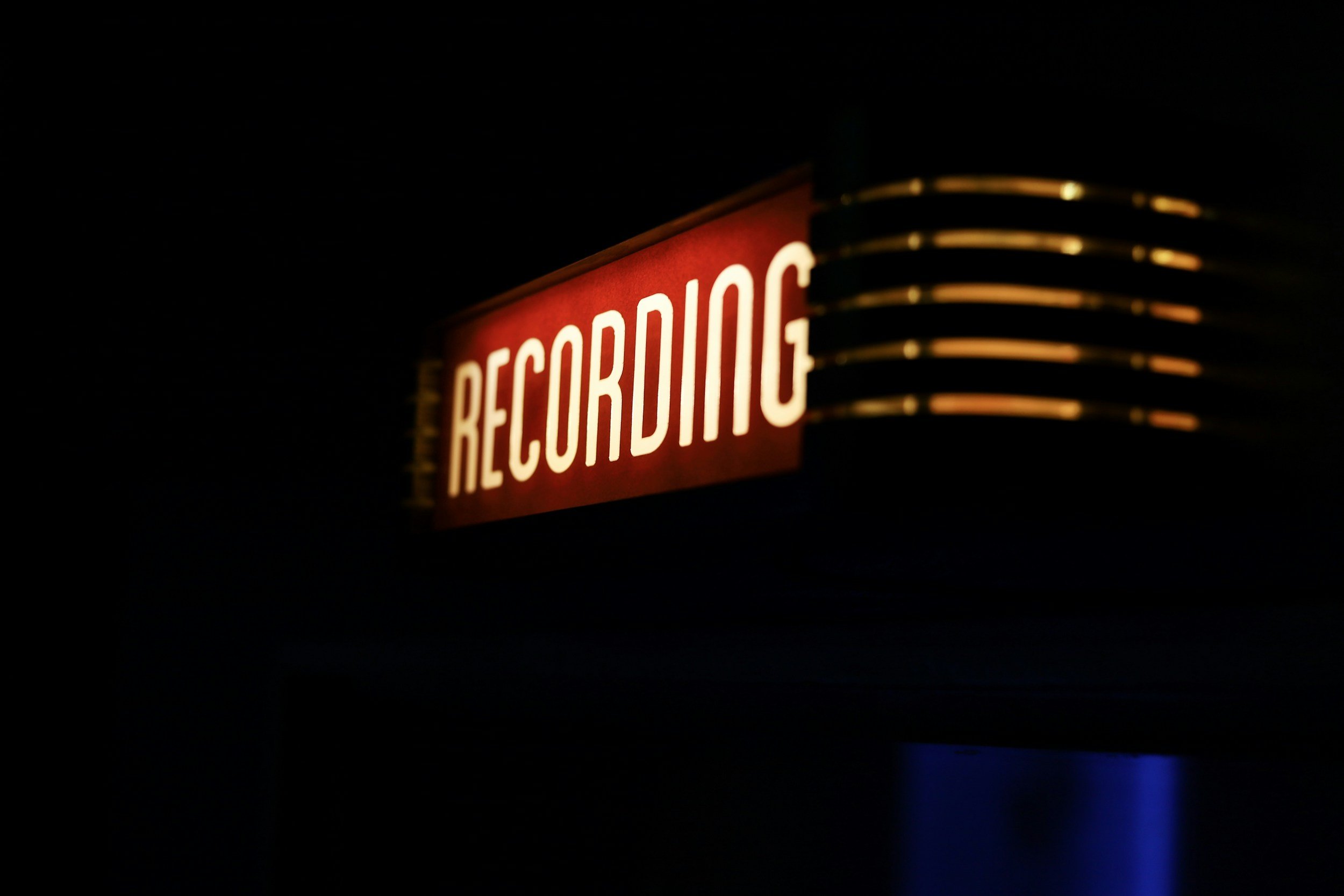 Un panneau lumineux rouge avec le mot 'RECORDING' écrit en blanc dans l'obscurité.