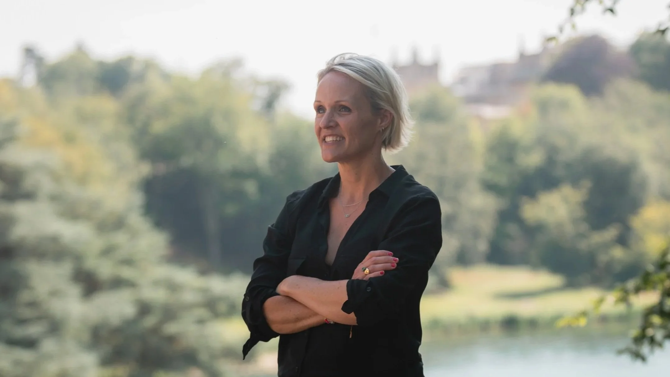 Nicola Graham, strategist, smiling arms folded with backdrop of foliage and buildings