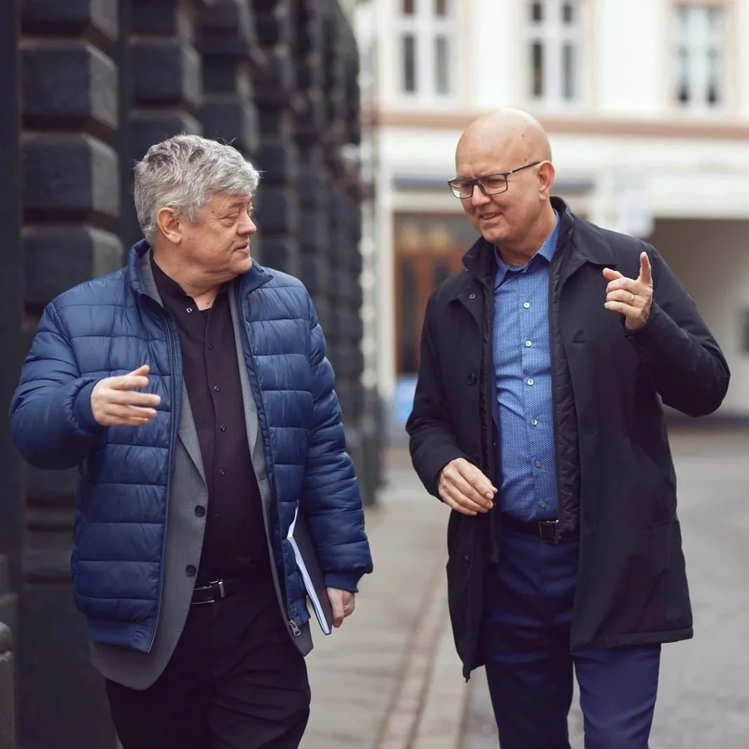 To mænd går og snakker på en fortov i en by