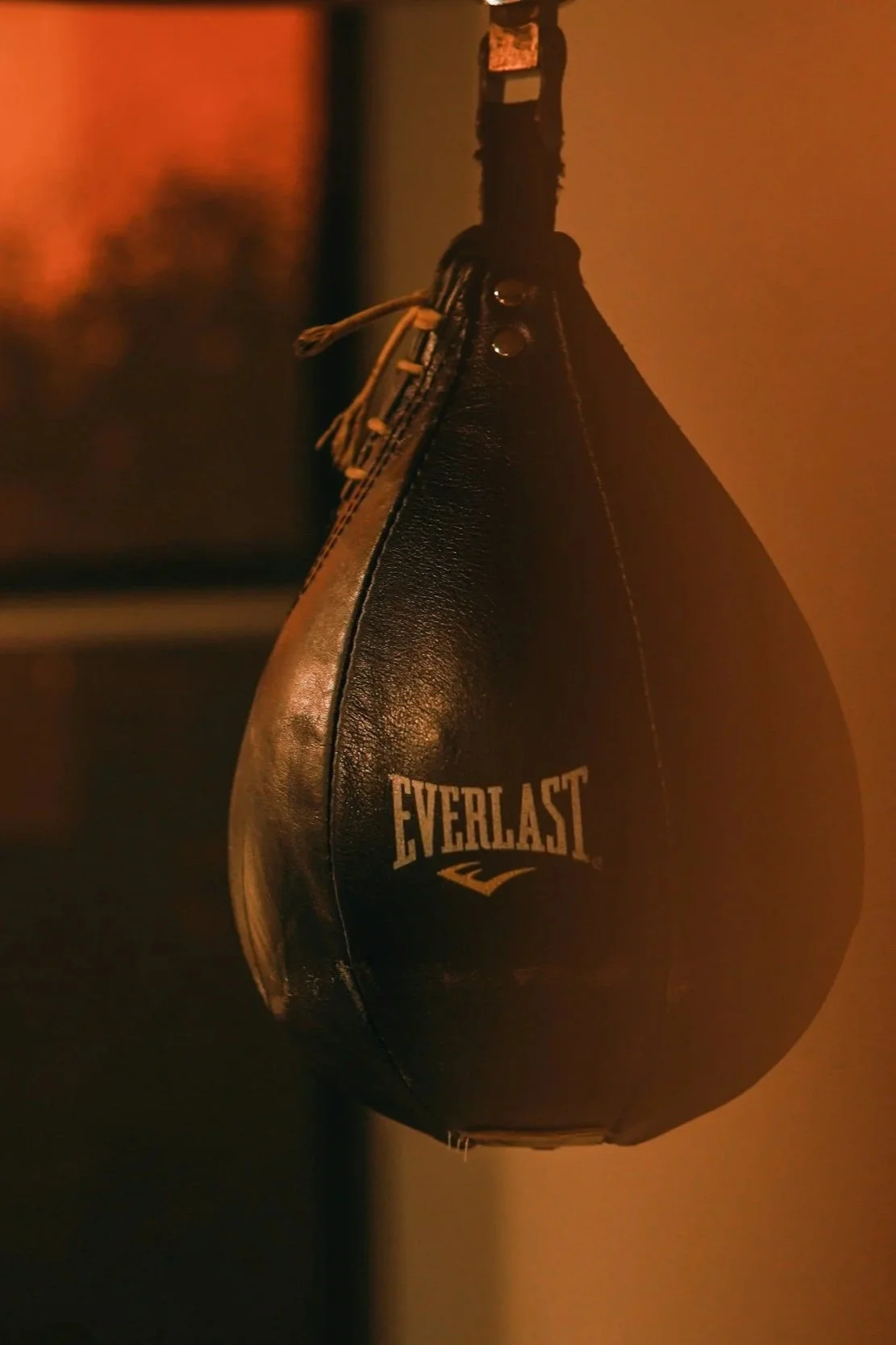 A black Everlast boxing speed bag hanging from a ceiling, with a tan lacing at the top and dim lighting.