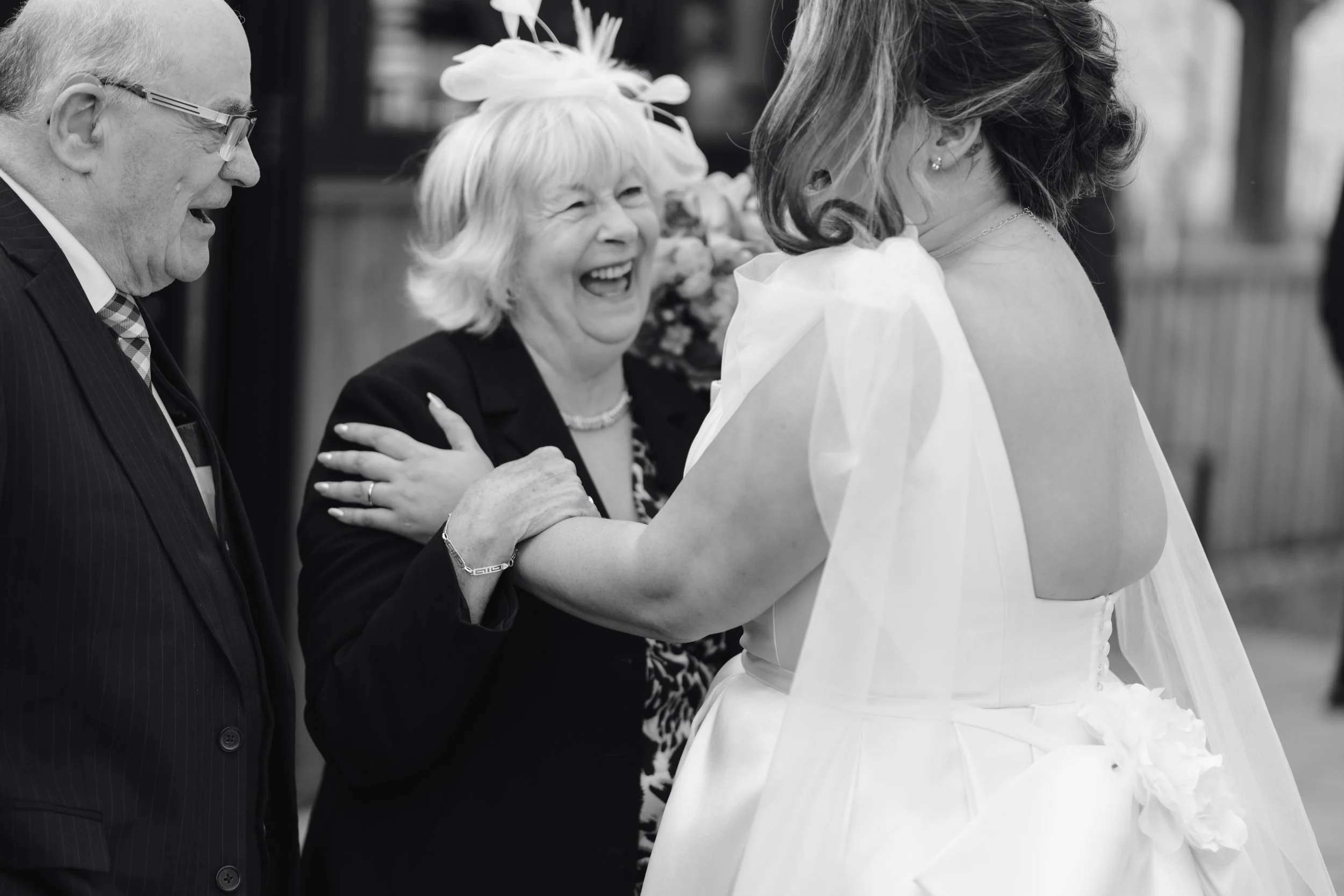 Three older adults and a bride smiling and talking at a wedding, with the bride in a white gown and the guests in formal attire.