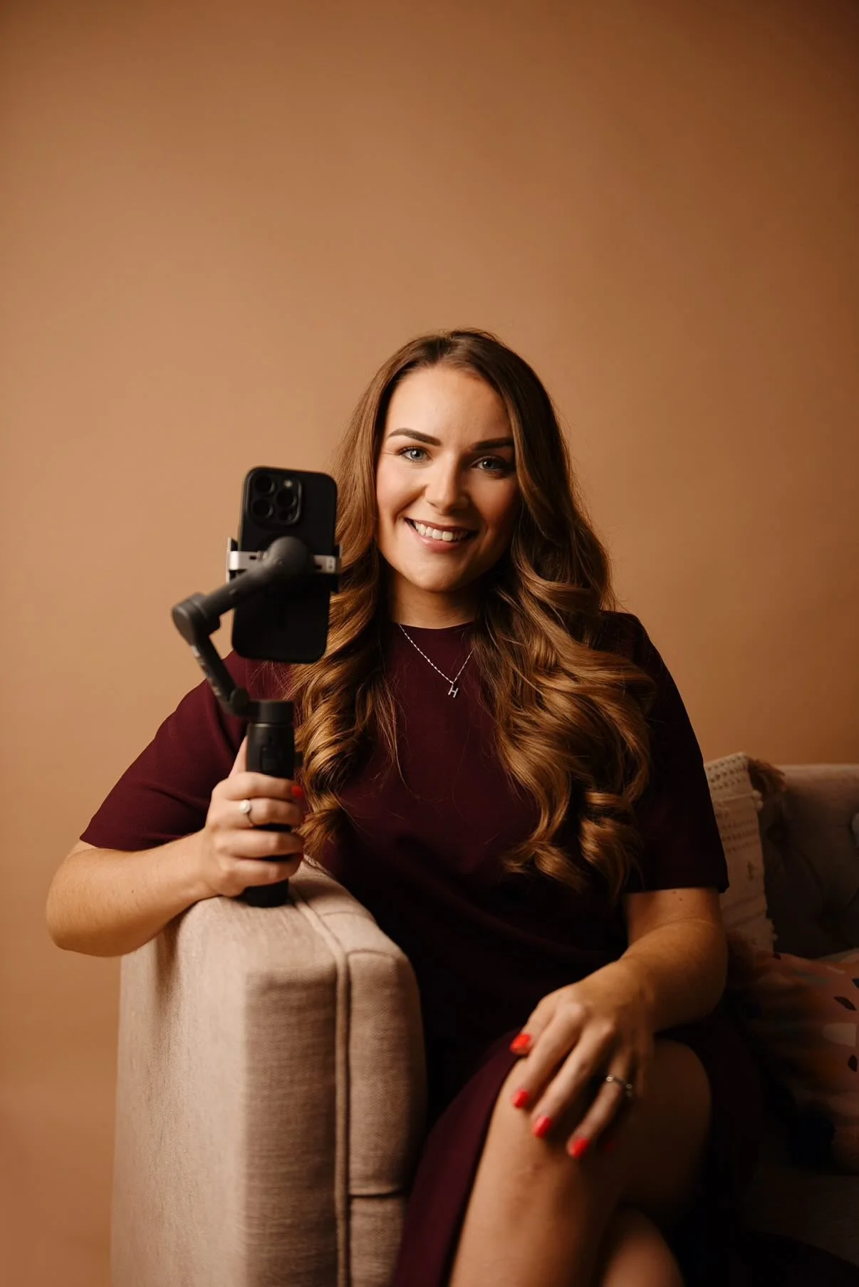 A woman smiling at the camera while holding a selfie stick with a smartphone attached.