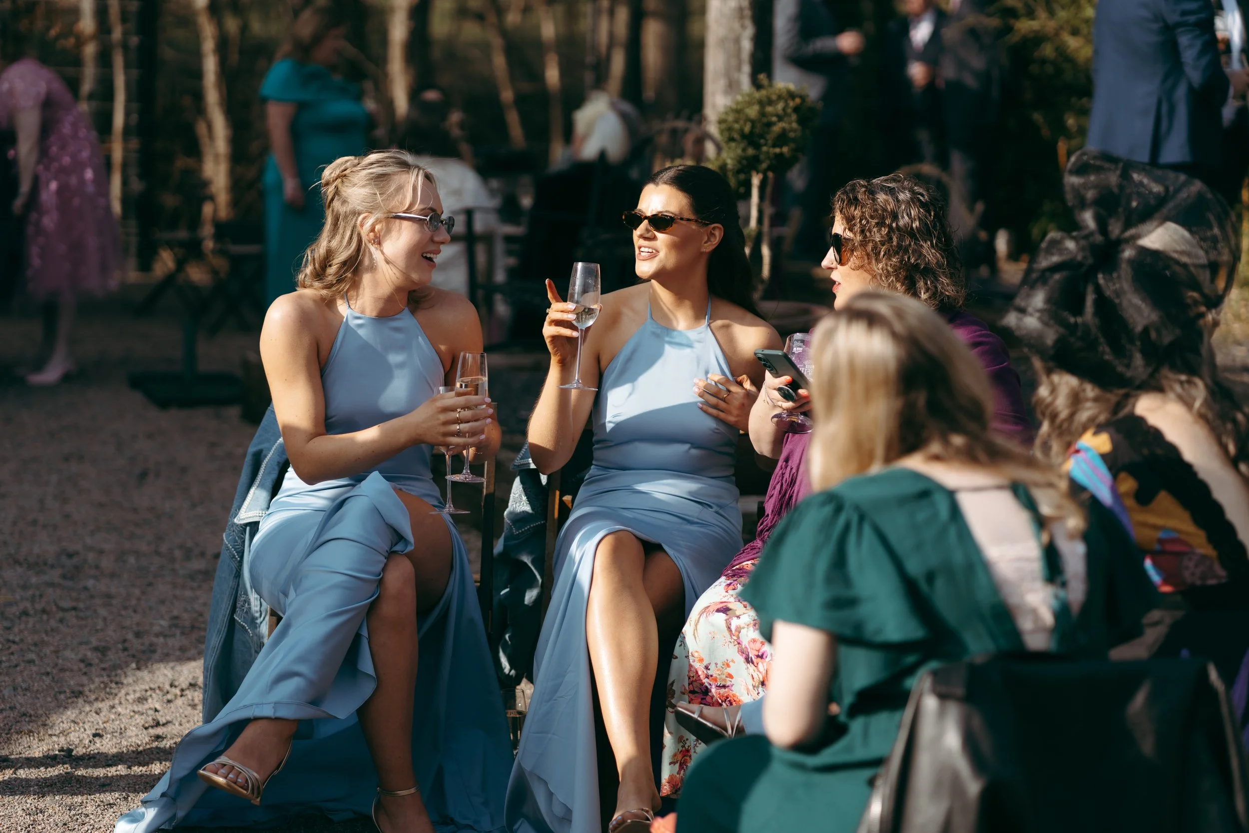 Group of women sitting outdoors, talking, and smiling, with some holding glasses of champagne during a social gathering or celebration.