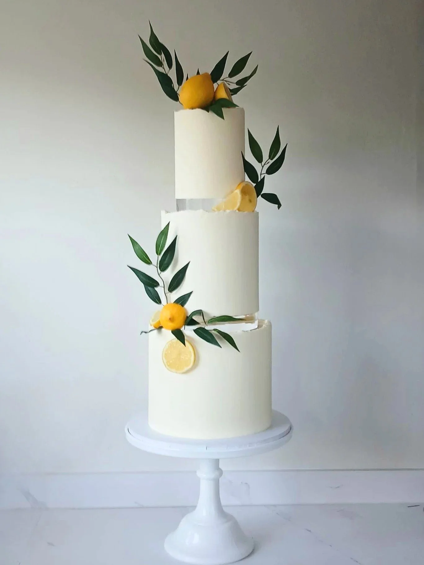 Three-tier white cake decorated with lemon slices and green leaves, placed on a white cake stand.