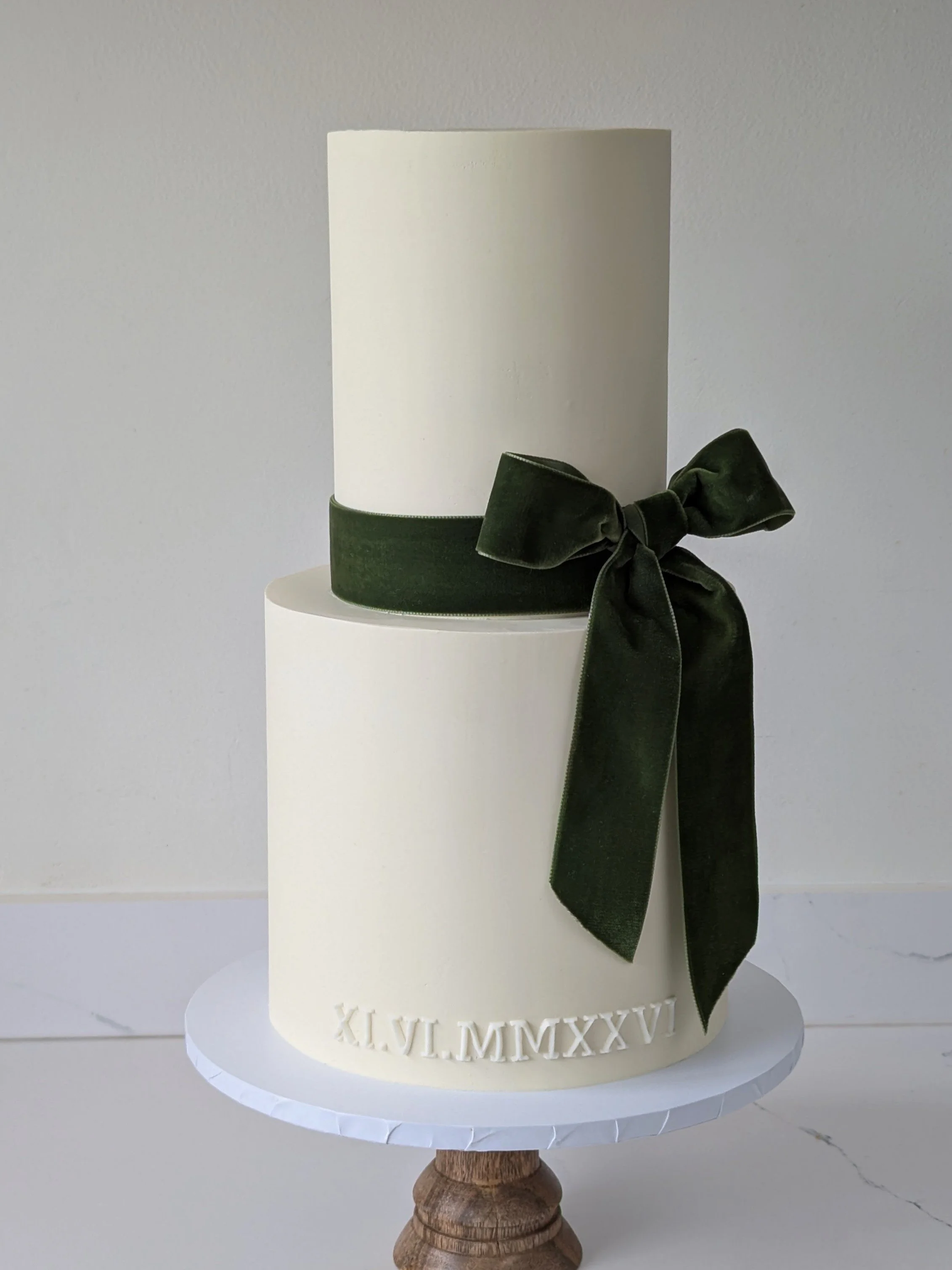 A classic and elegant two tier wedding cake with velvet dark green bow, and the wedding date in roman numerals. 
