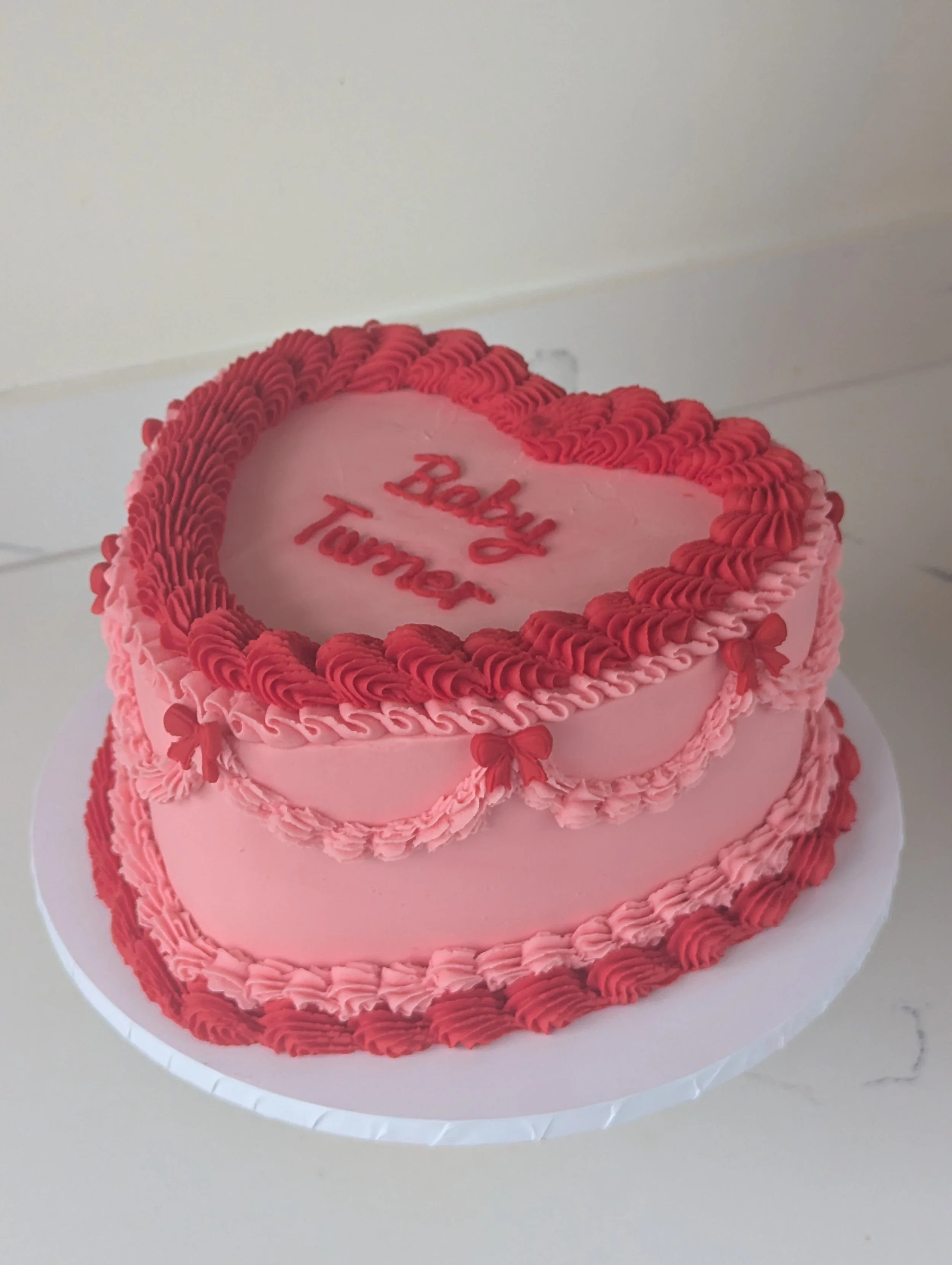 Heart-shaped pink cake with red and pink frosting details and a message that reads 'Baby Tummy'
