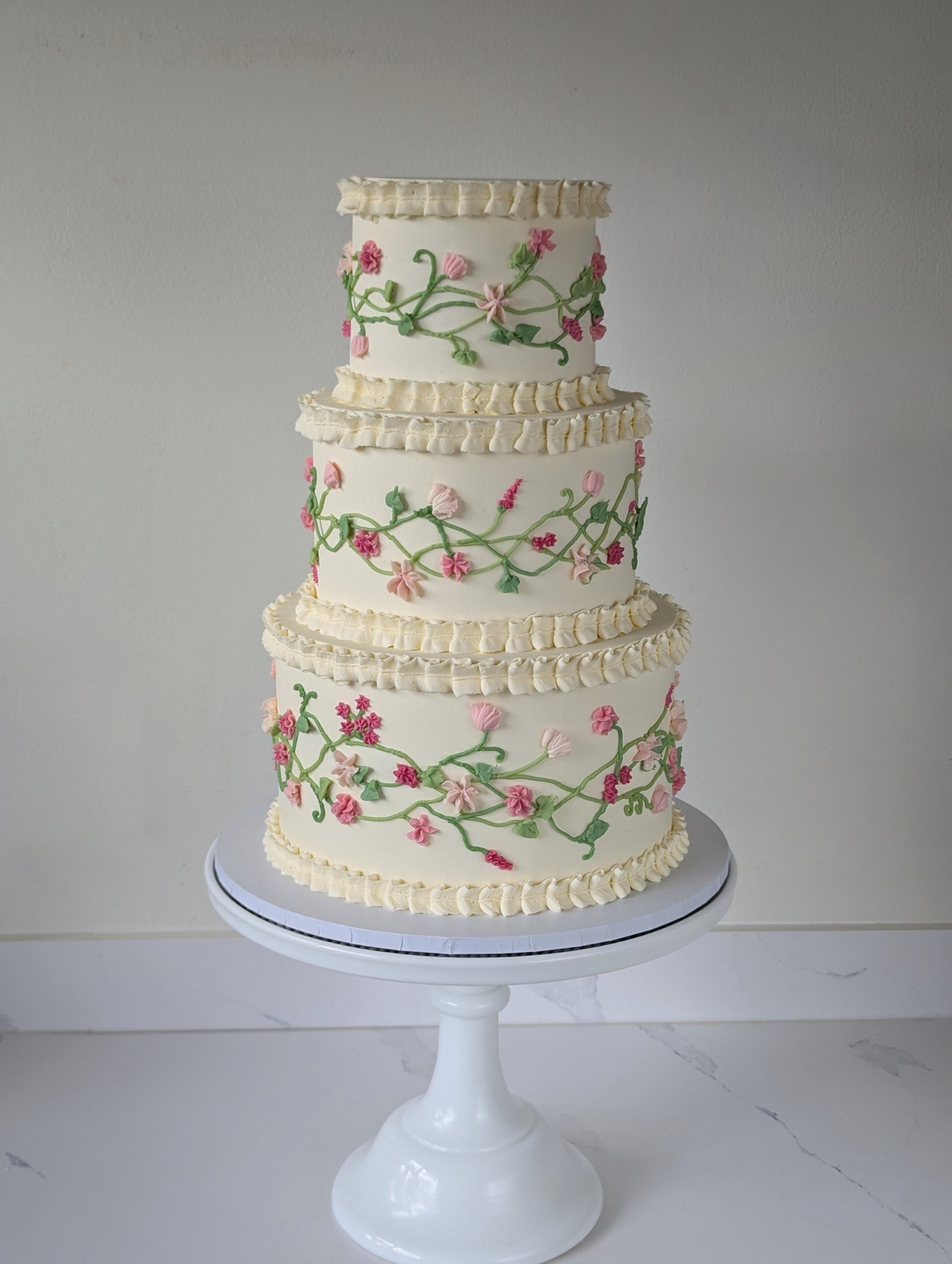 Three tier wedding cake with piped ruffles and flowers. 