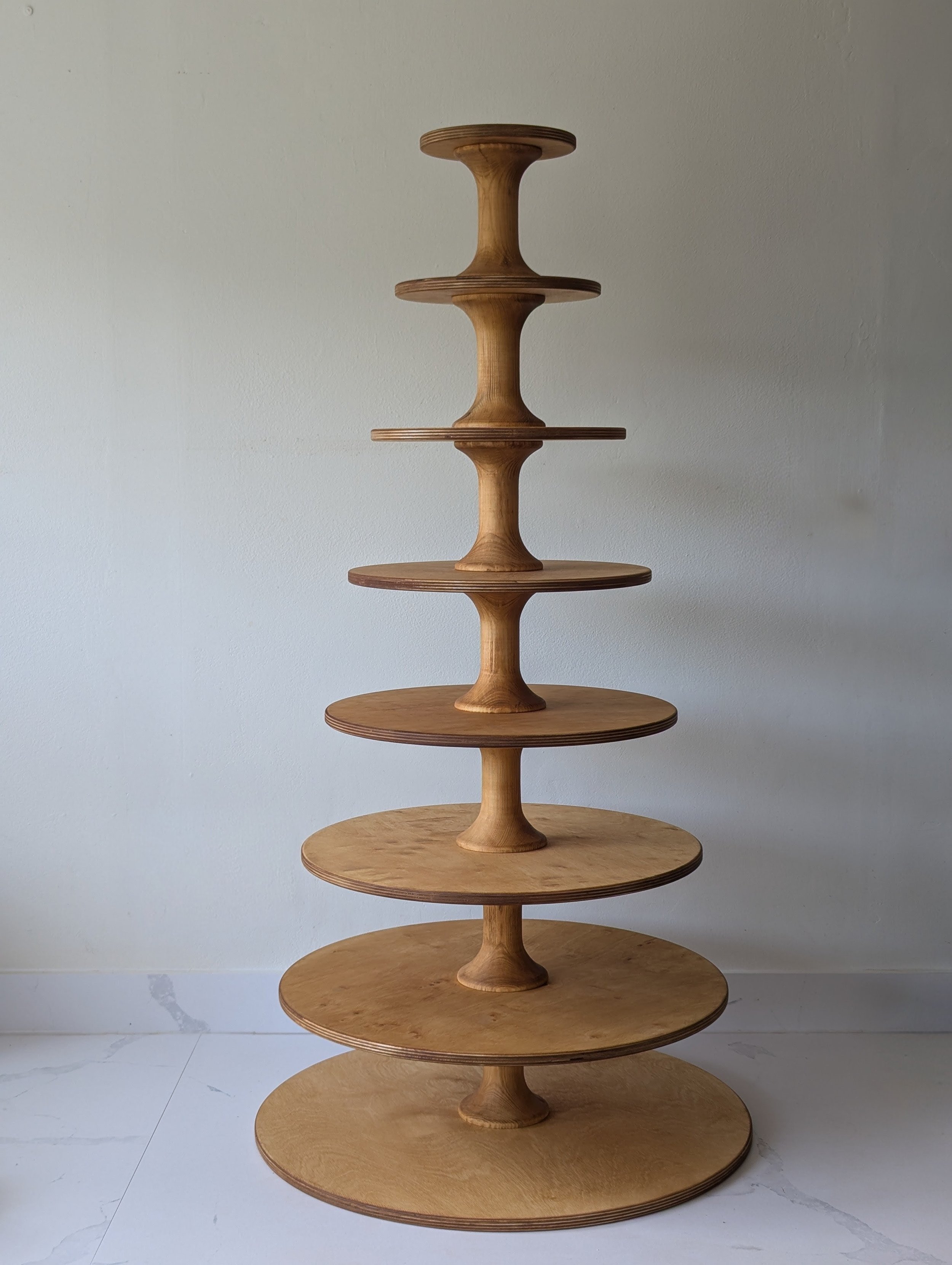 A wooden display stand with multiple circular tiers connected by vertical supports, arranged in a tiered fashion against a plain wall.