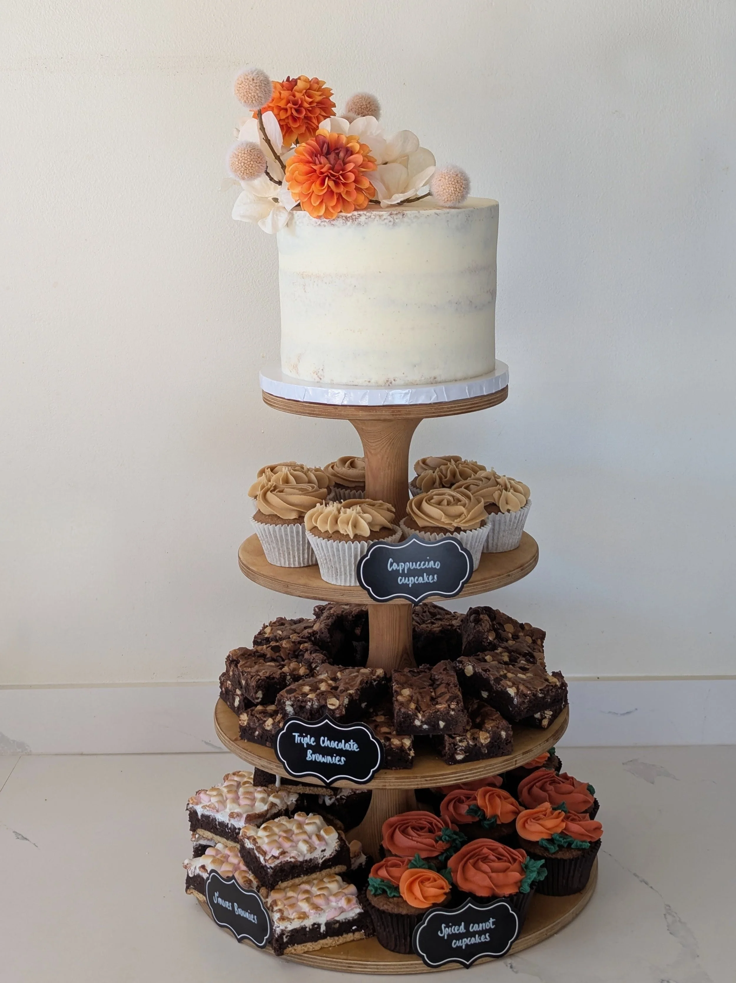 A multi-tiered dessert display with a variety of baked goods, including a decorated cake on the top, cupcakes around the middle, chocolate brownies on the next tier, other brownies on the bottom, and decorated cookies. A wedding at Bowerchalke Barn. 