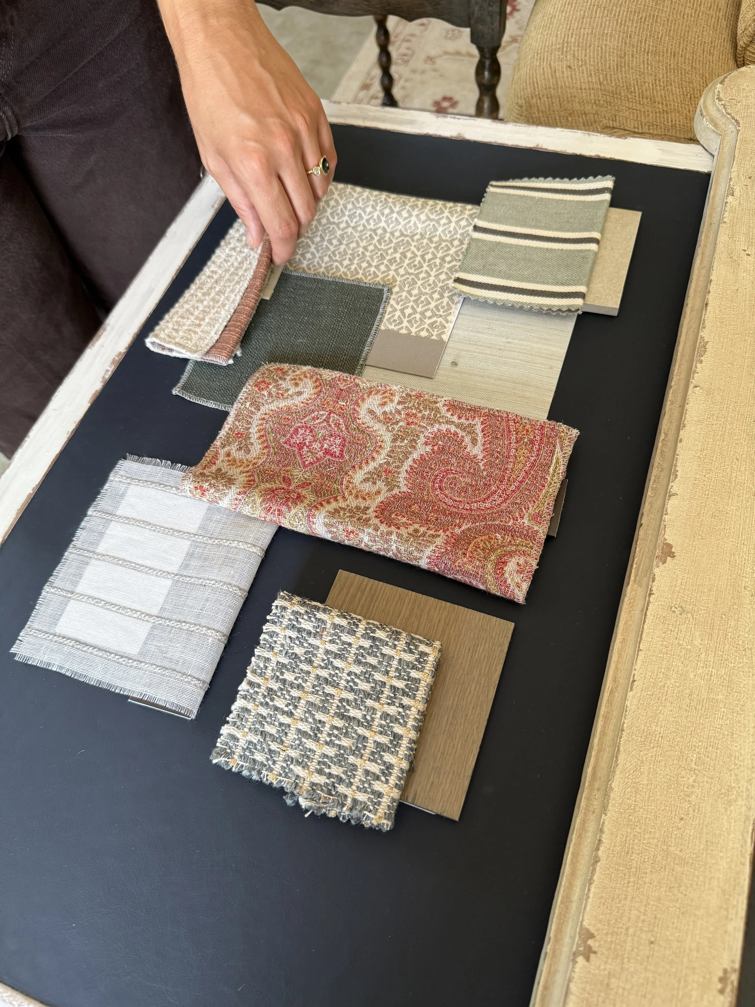 Person's hand holding fabric samples with various textures and patterns, placed on a black surface.