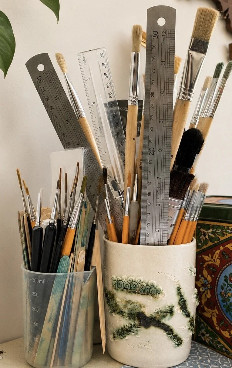 A collection of paintbrushes and rulers in two containers on a table.