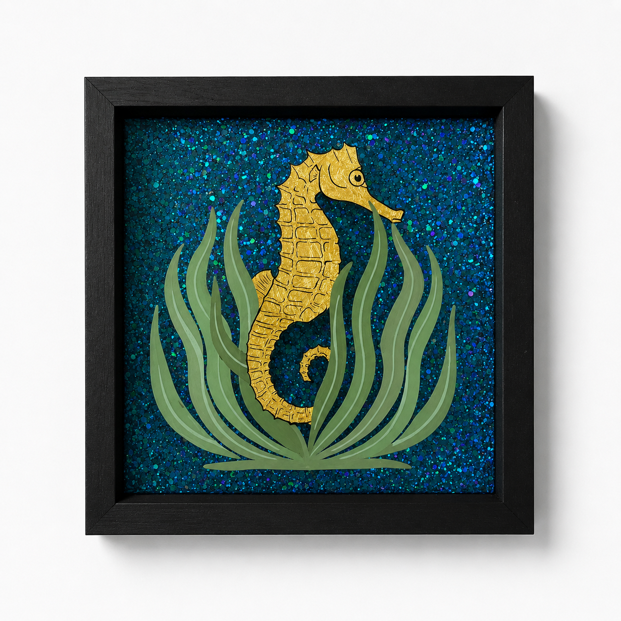 A framed artwork of a yellow seahorse surrounded by green seaweed, with a background of blue and purple glitter.