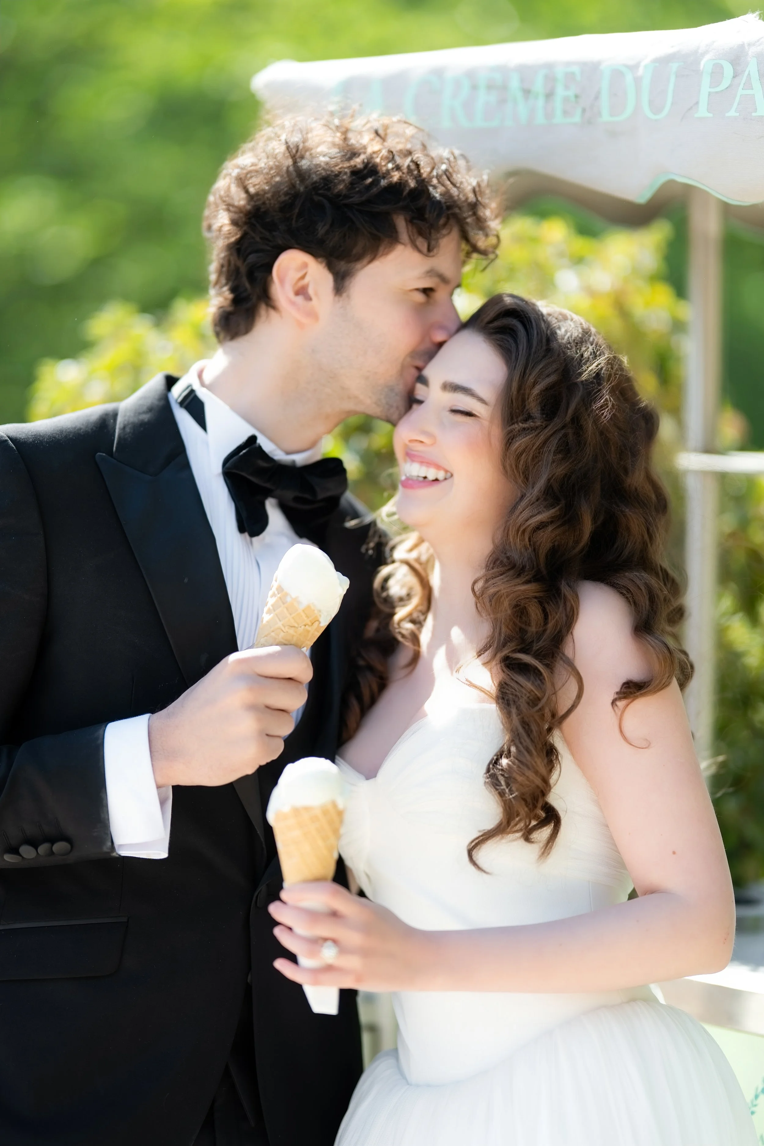 A bride and groom sharing a kiss outdoors during their wedding, both holding ice cream cones.