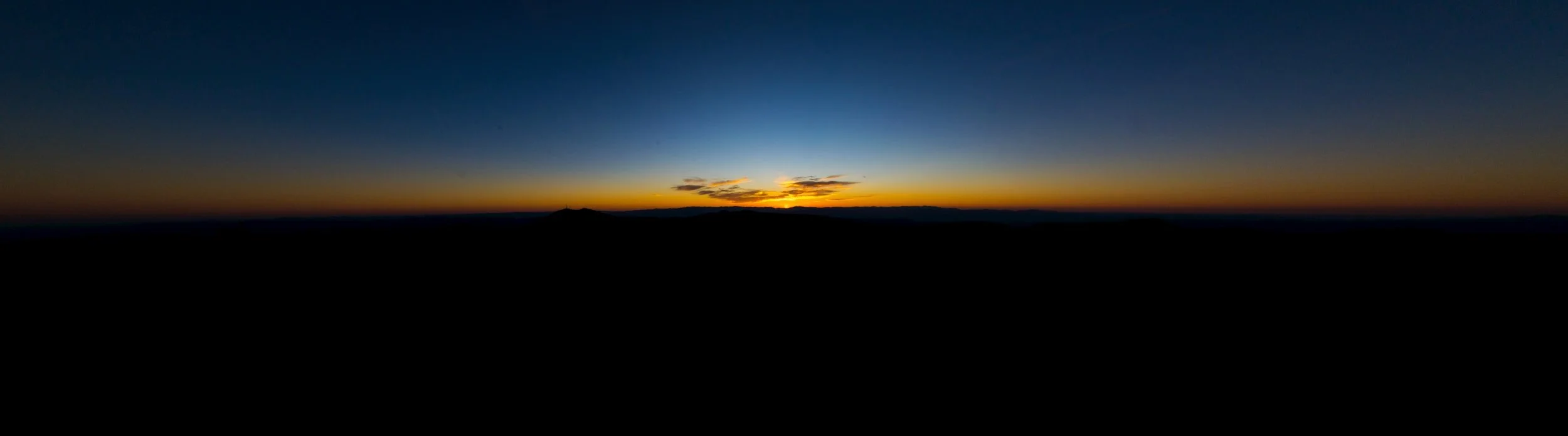 A vivid sunset over a silhouette of distant mountains with a clear sky transitioning from light to dark.