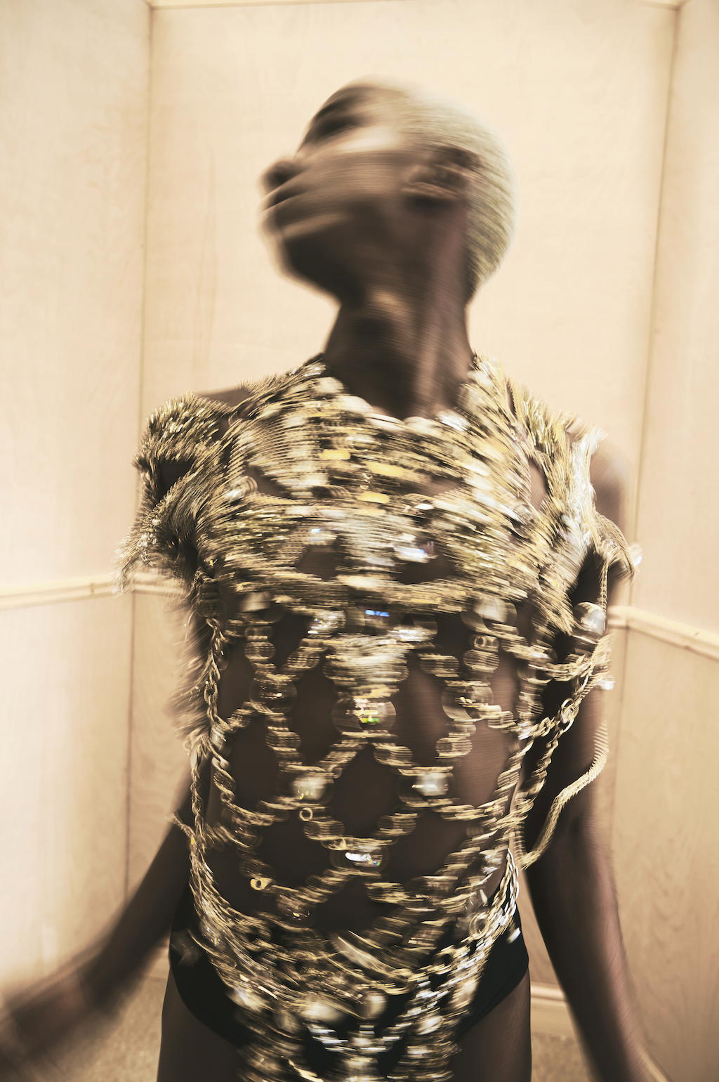 Person wearing a black dress with intricate gold and silver beaded detailing, standing in a beige-walled room