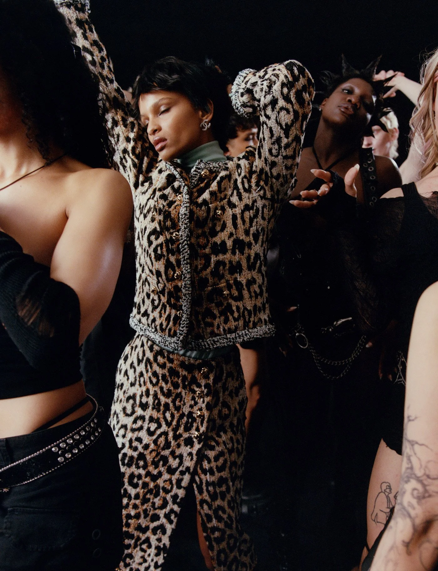 People dancing closely in a dark environment, with one woman wearing a leopard print outfit and others in dark clothing.