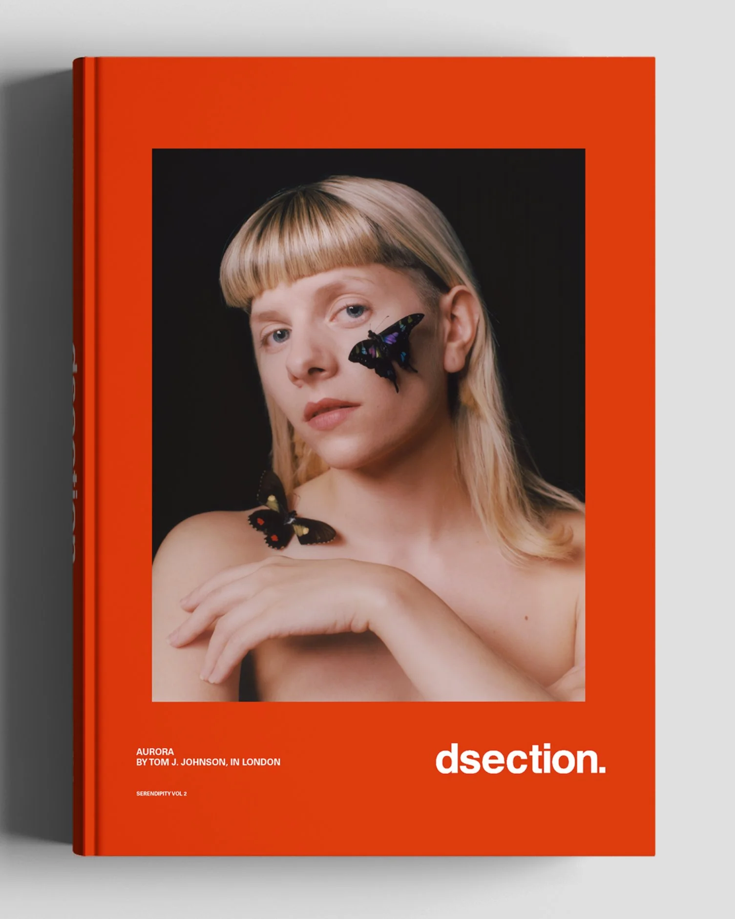 A book cover with a portrait of a young woman with long blonde hair, blue eyes, and a butterfly on her cheek and shoulder, set against a dark background. The cover has a red border and white text at the bottom.