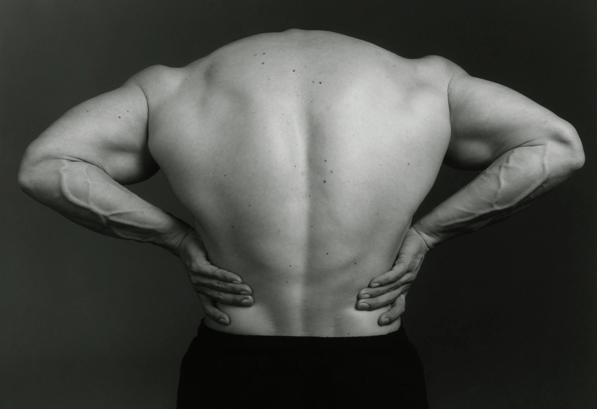 Black and white photo of a person with a bare back, hands on hips, and their face outside the frame.