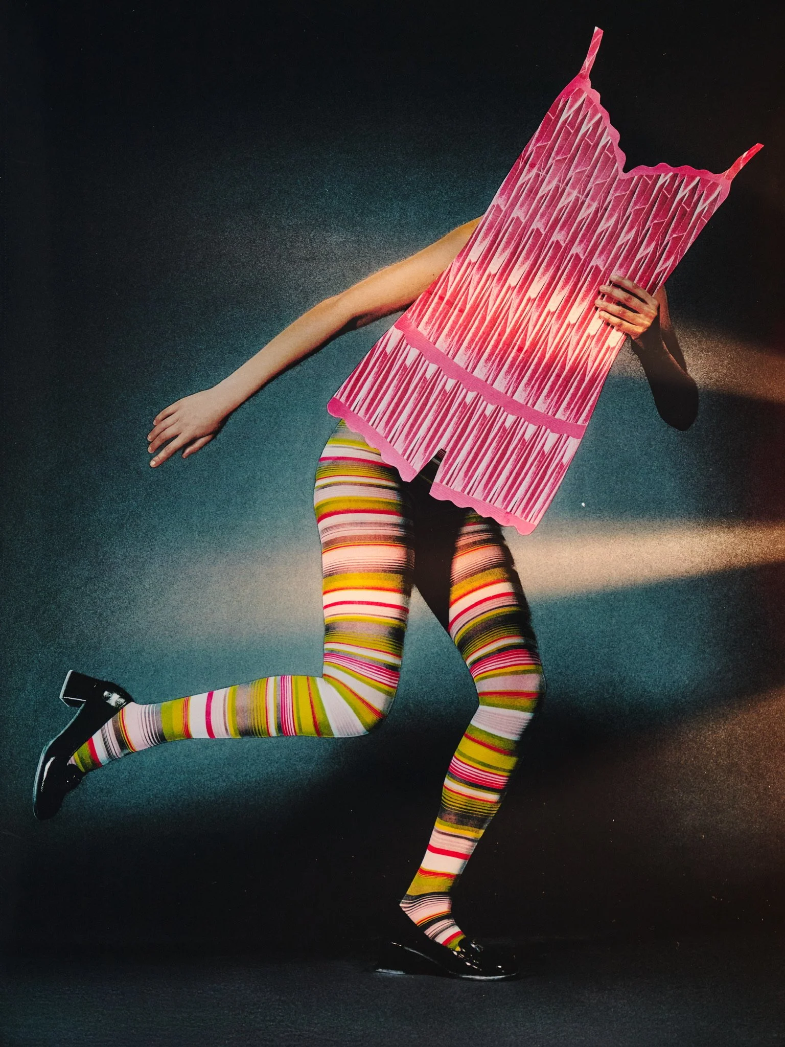A person dressed in colorful striped leggings and black shoes is holding a pink and white striped paper bag over their face while jumping against a dark background.