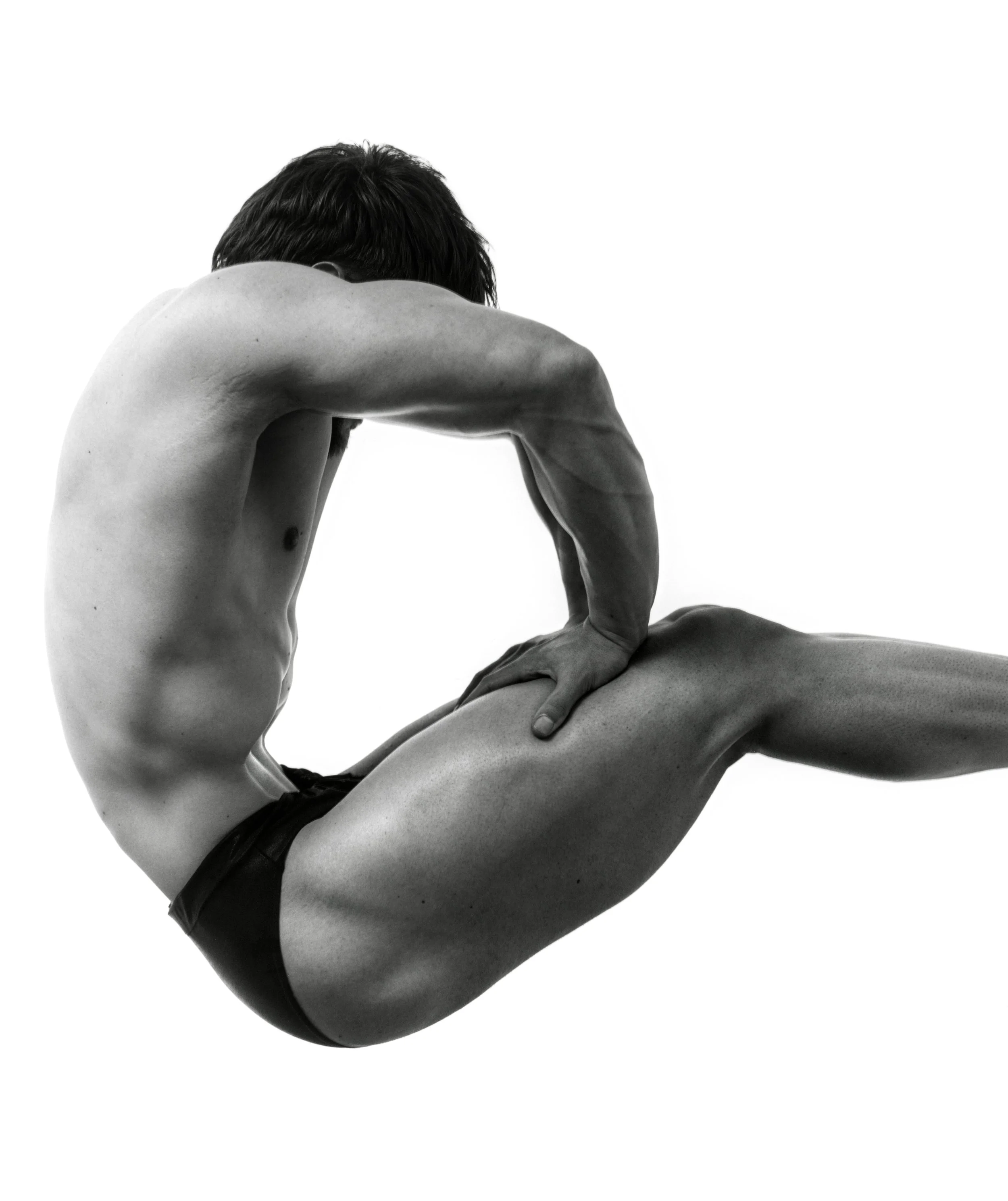Black and white photo of a shirtless man with dark hair, bent forward with his head resting on his bent arm, showcasing his muscular back and arm.