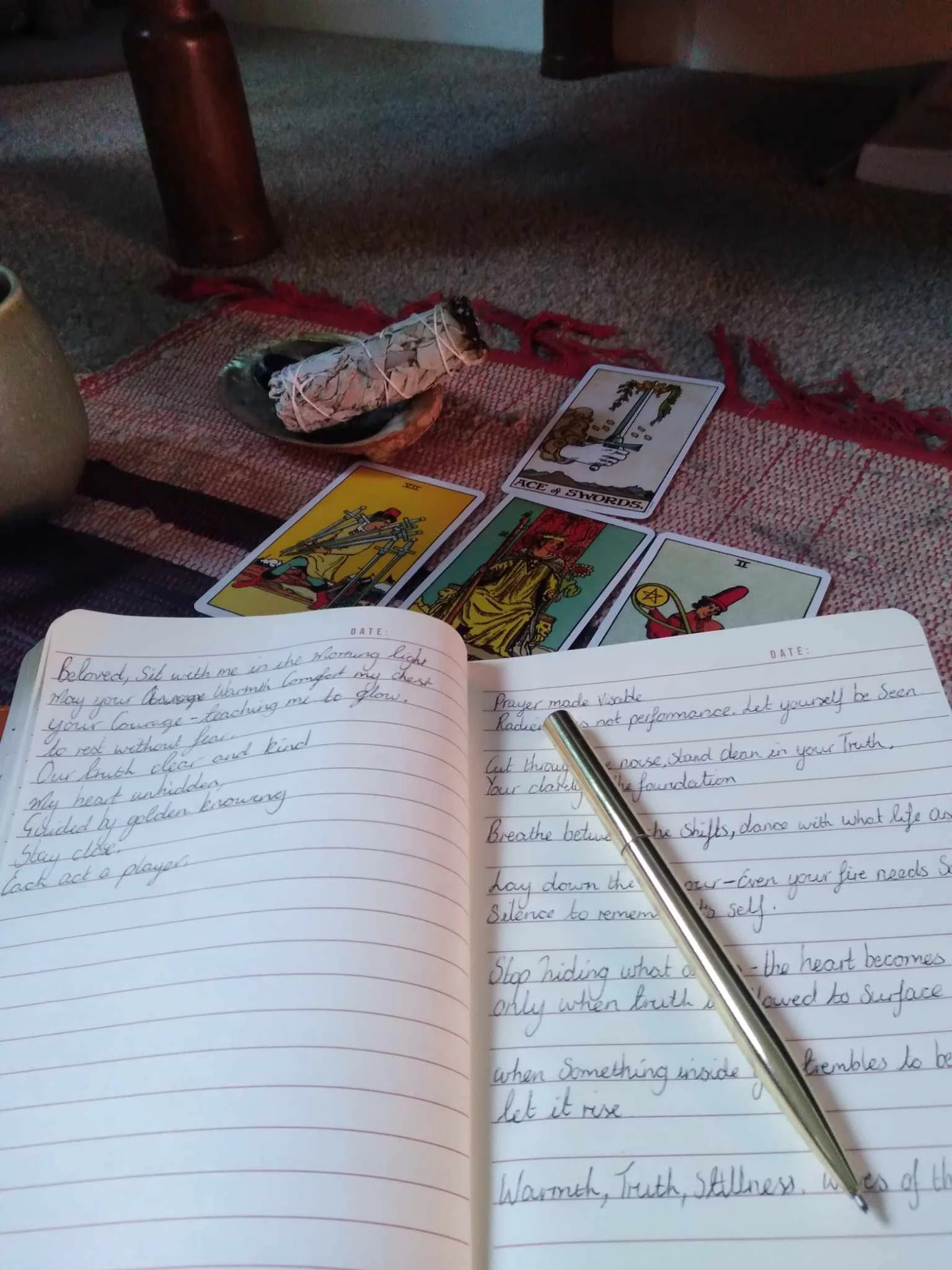 Open notebook with handwritten notes, a pen resting on the pages, tarot cards near the top of the pages, and a small smudge of ink on the words.