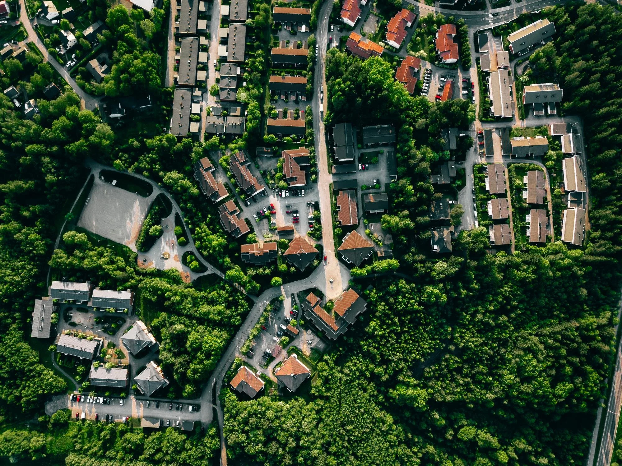 Aerial view of a residential neighborhood with houses, trees, streets, and parked cars.